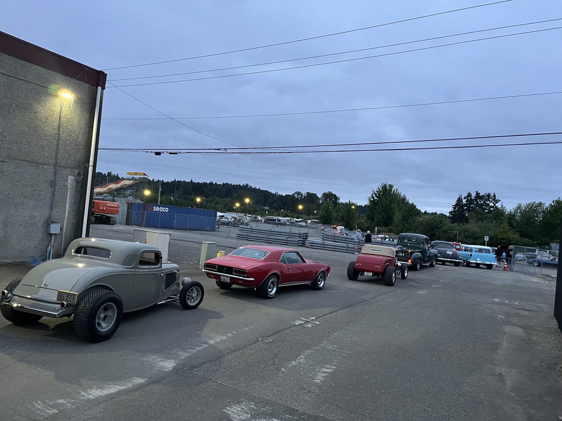 Row of classic cars parked in a lot at dusk under cloudy sky