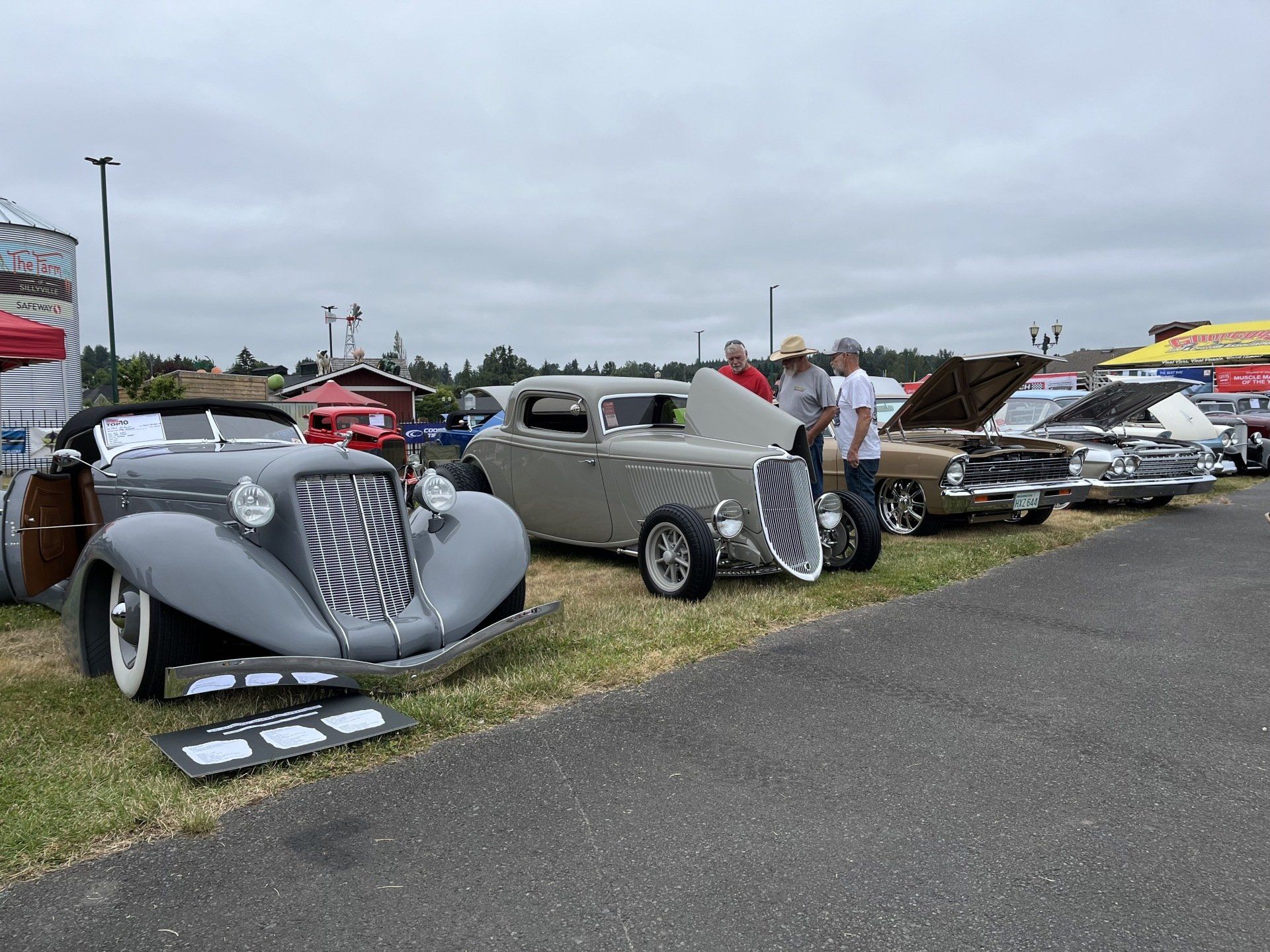 Classic custom cars lined up at an outdoor show on a cloudy day.