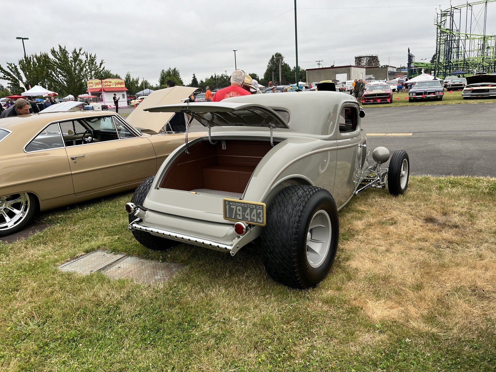 Gray vintage hot rod parked on grass at an outdoor car show, rear three-quarter view