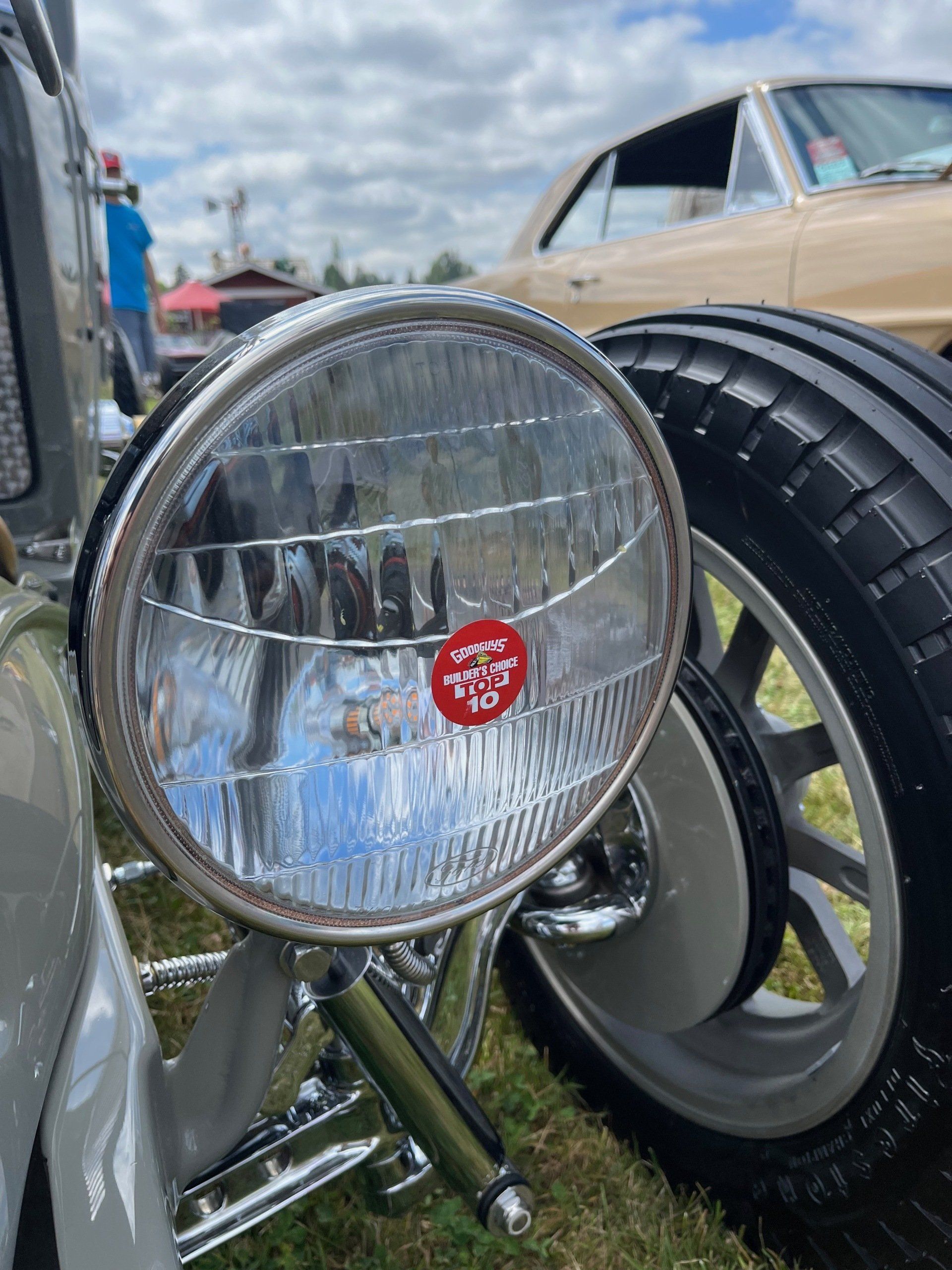 Close-up of a chrome vintage car headlight beside a black tire under a cloudy sky