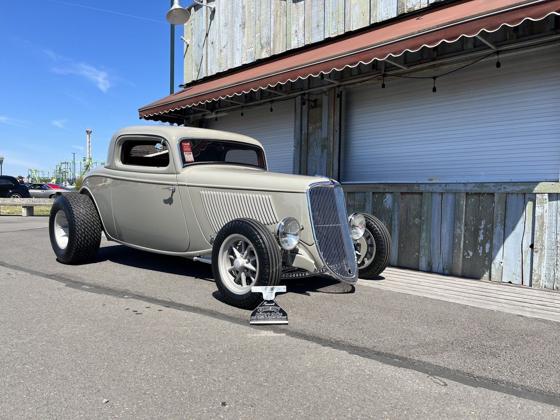 Vintage gray hot rod parked by a building on a sunny street.