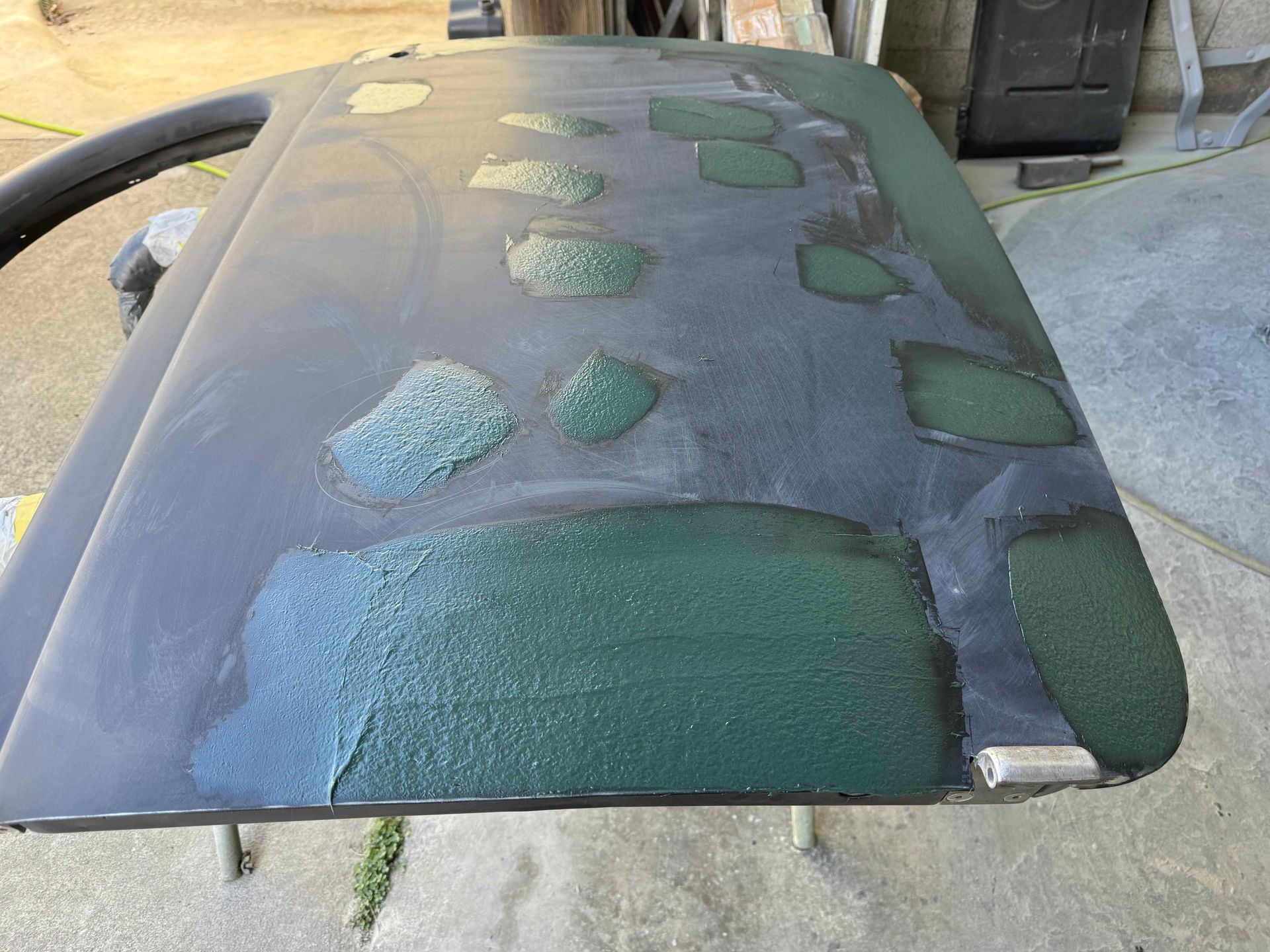 Car hood with multiple green and blue sanding patches, showing bodywork repair in progress
