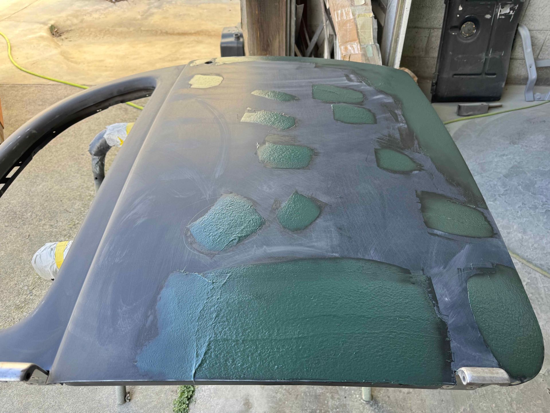 Damaged green car hood with large scratches and peeling paint in a garage