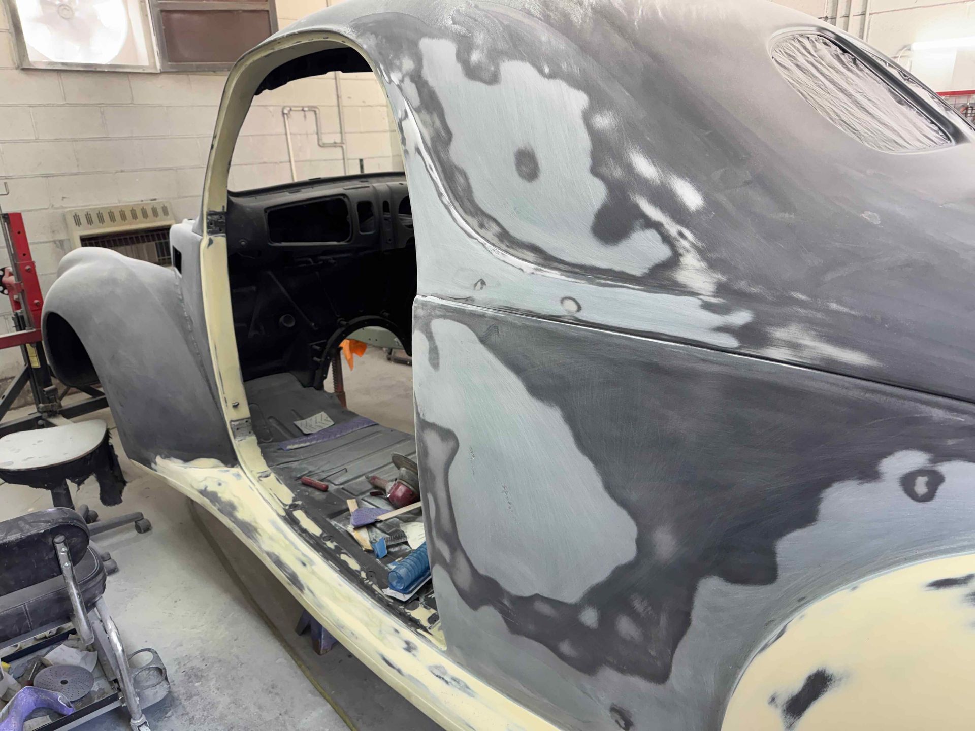 Classic car body in a garage, stripped for repair and covered in gray primer patches