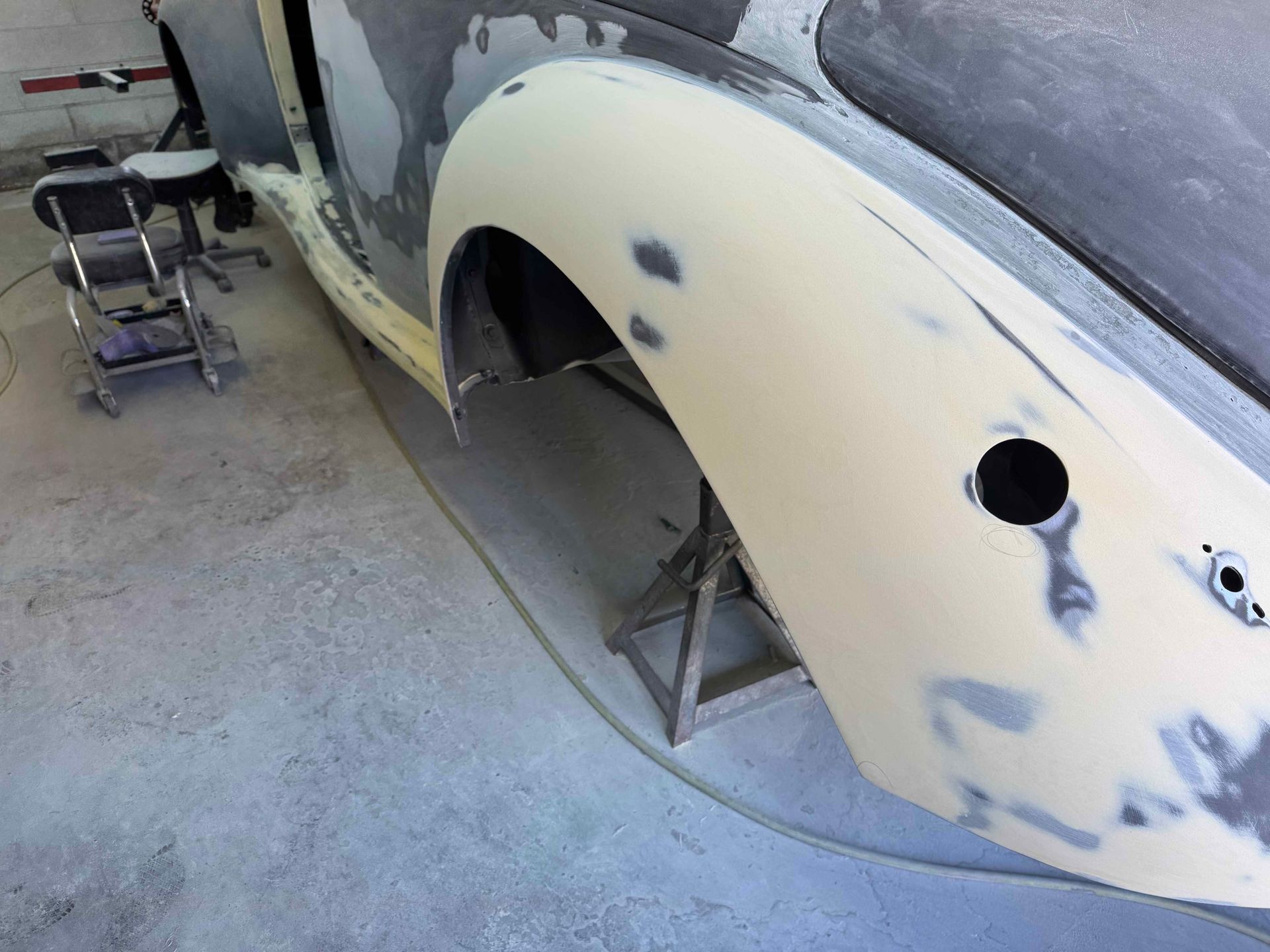 Partially primed car body in a workshop with sanding patches and a wheel well opening