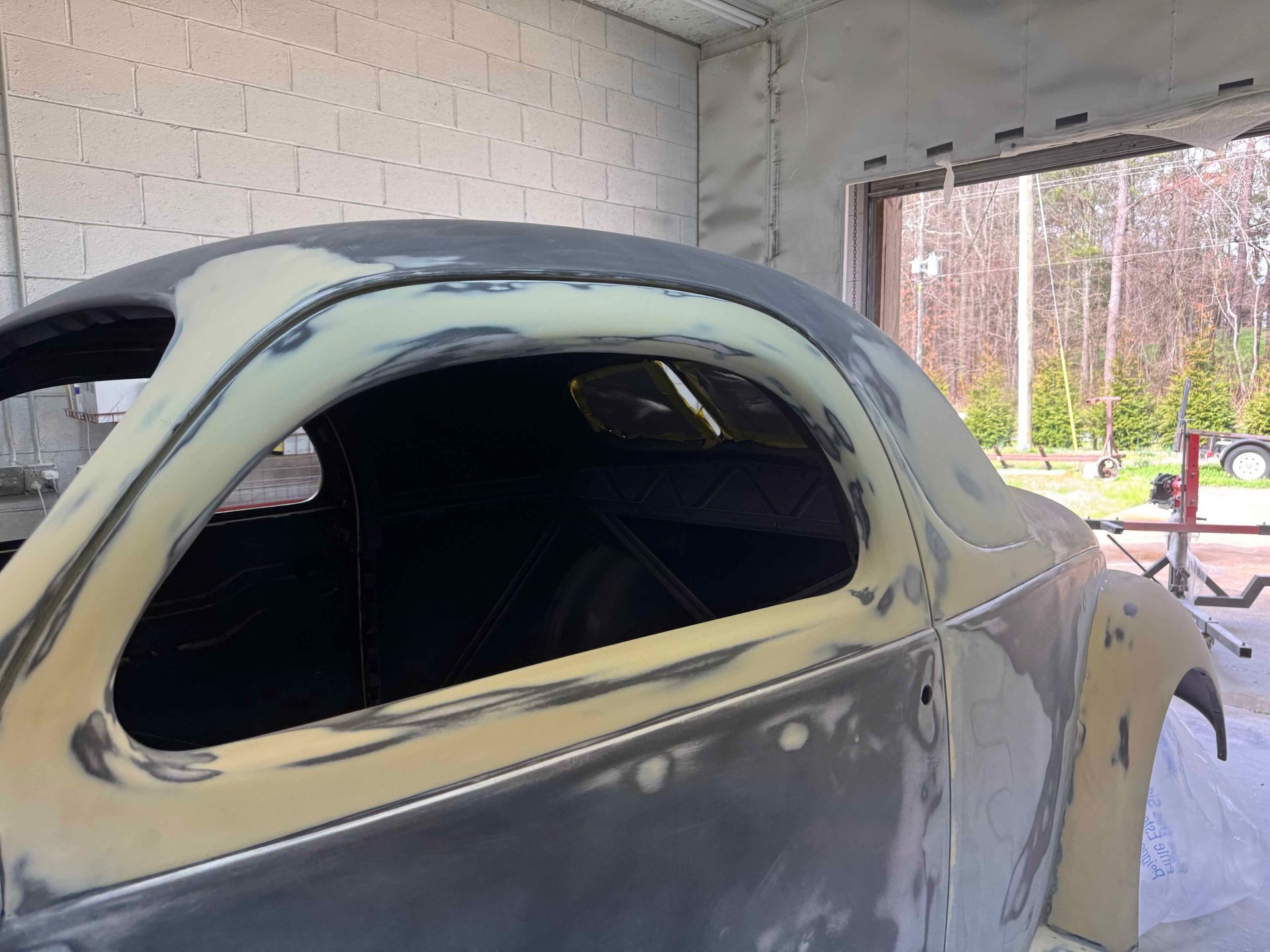 Primered vintage car body in a garage, with windows masked out and bodywork in progress.
