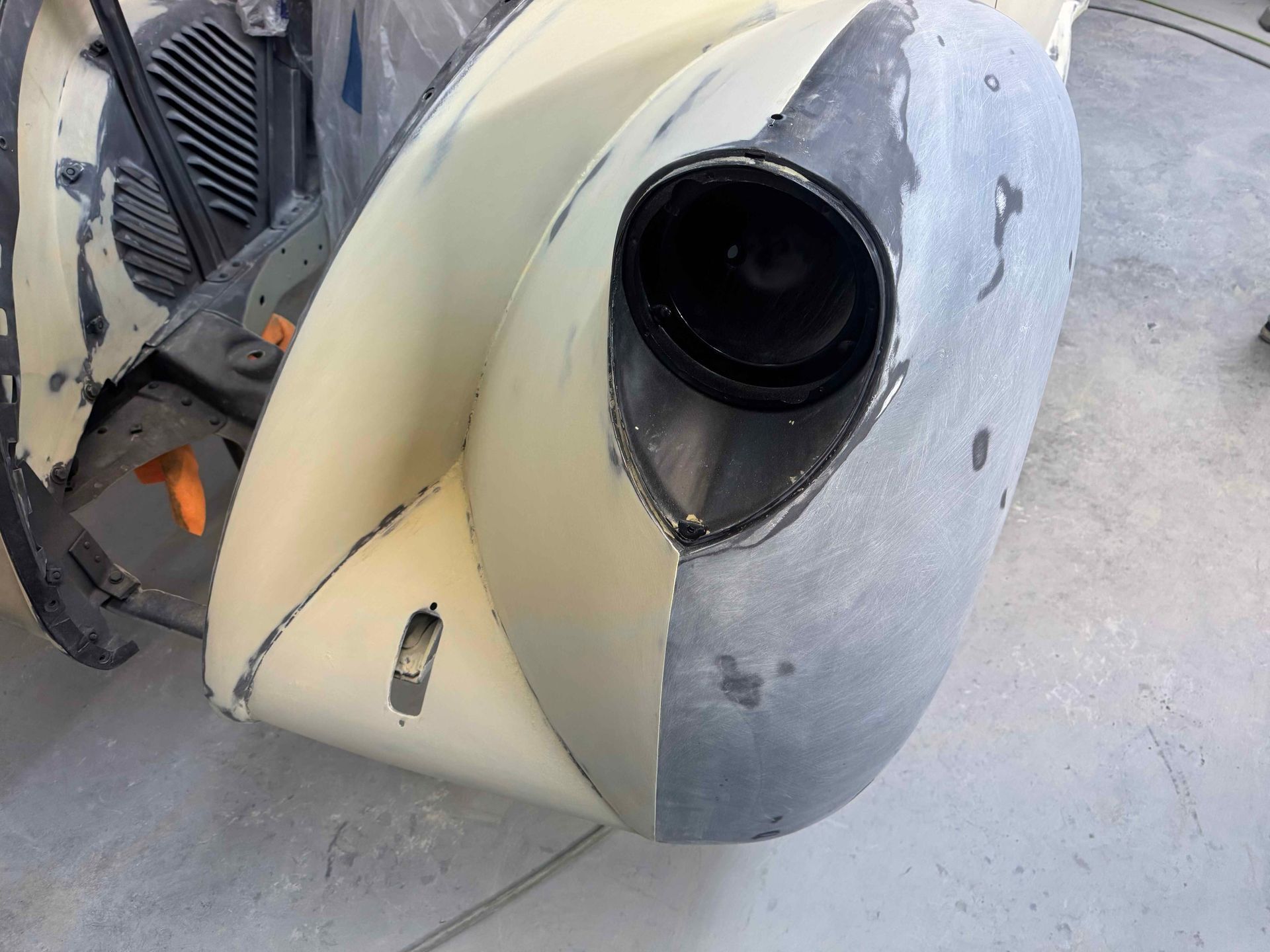 Painted metal car body panel with a large circular opening and gray primer, resting on a concrete floor