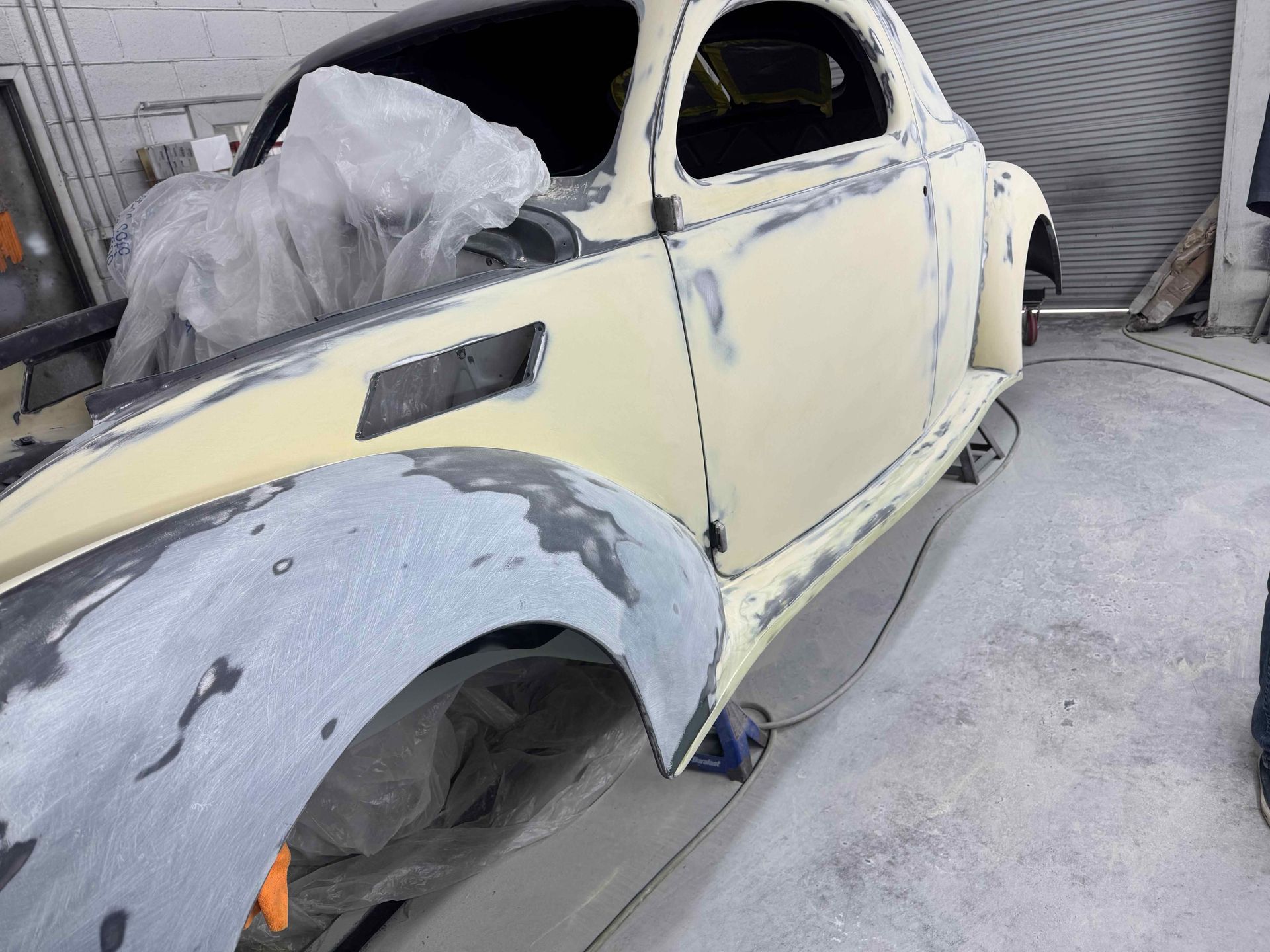 Partially restored cream vintage car body in a garage, with gray primer on the fenders