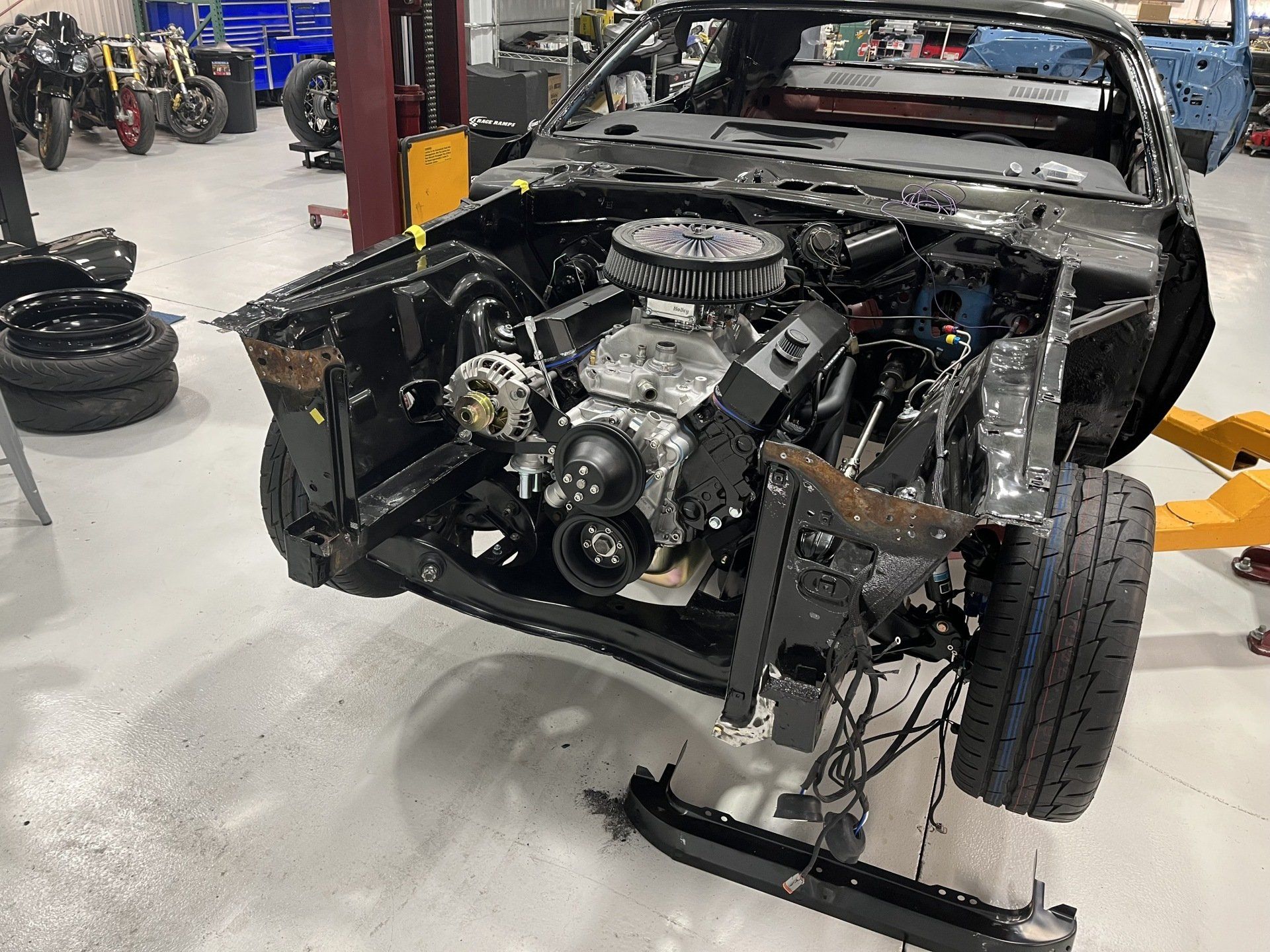 Partially disassembled black car chassis in a workshop, showing exposed engine and front-end components