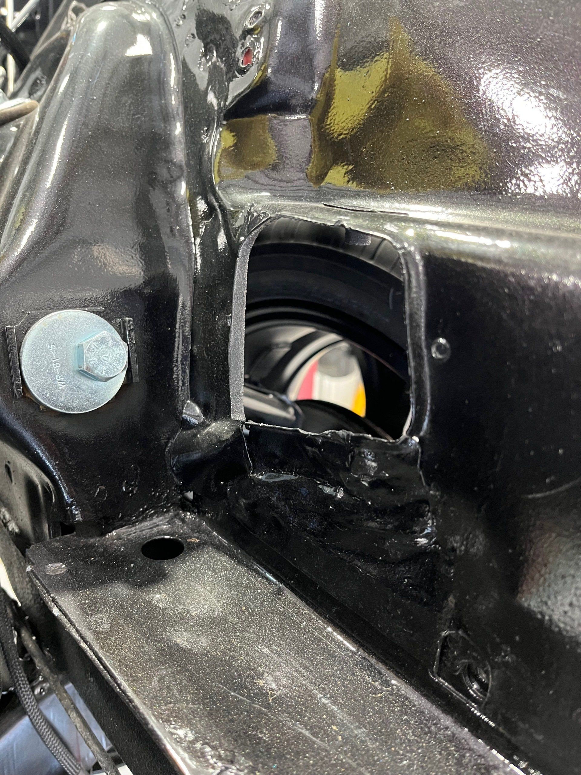 Close-up of a black metal bracket with a silver bolt and a circular opening showing a gray cable inside.