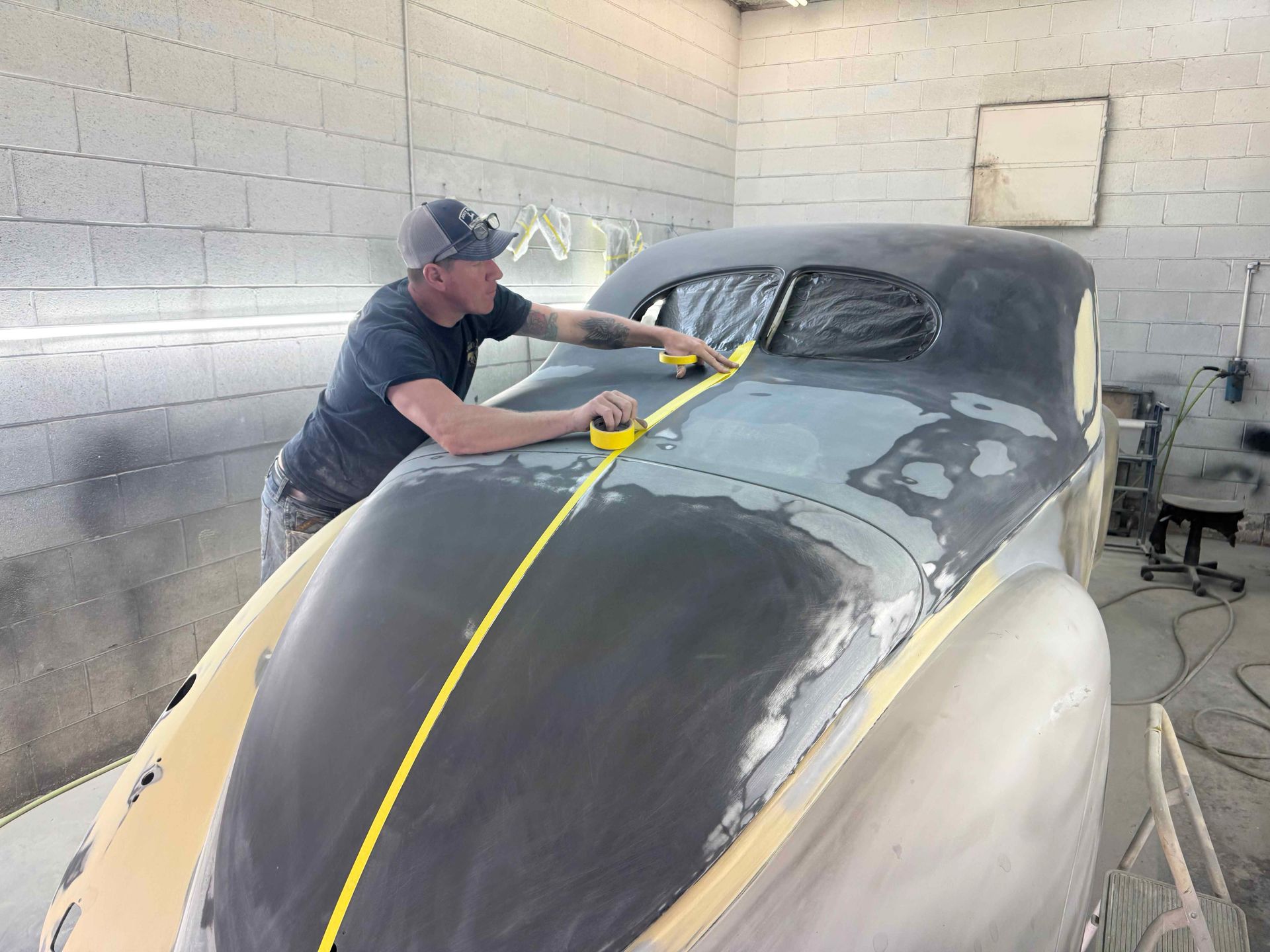 Worker sanding a gray car body in a garage workshop