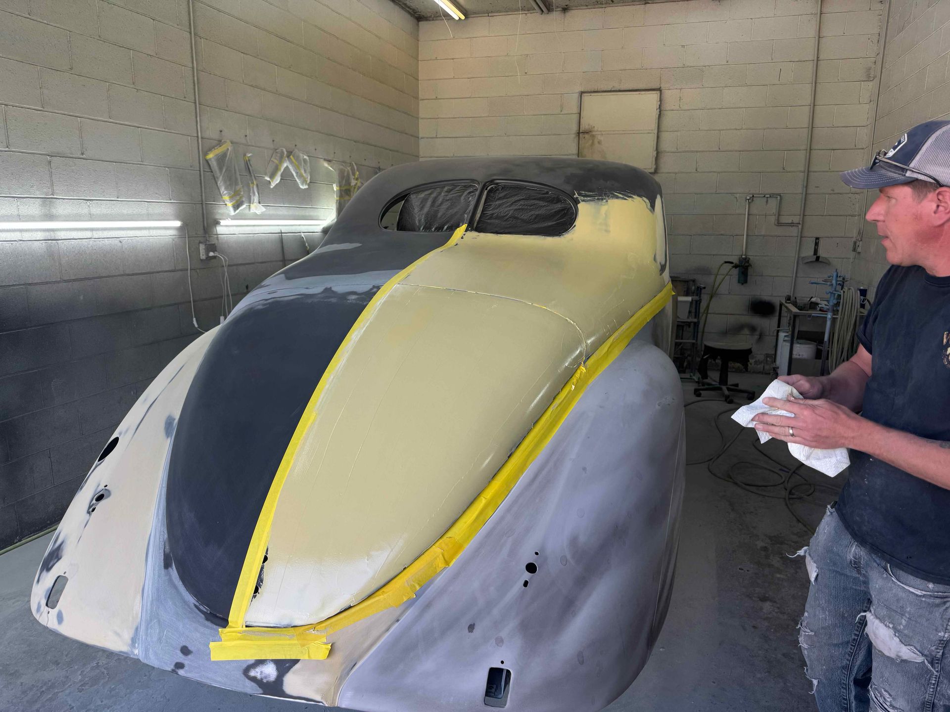 Custom car body in a workshop, gray with black and yellow stripes, with a man standing beside it.