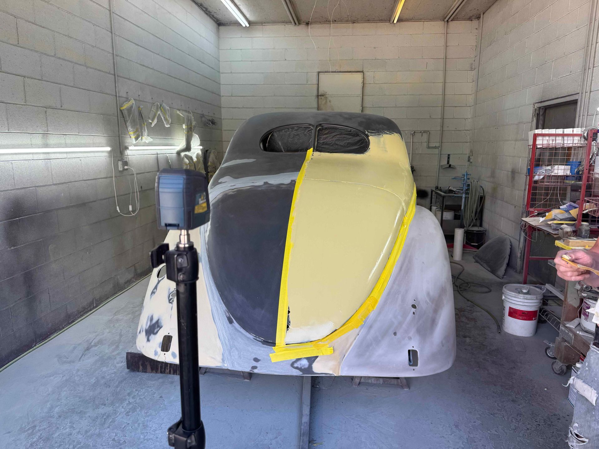 Partially painted car in a garage, with yellow masking tape and gray primer on the front.