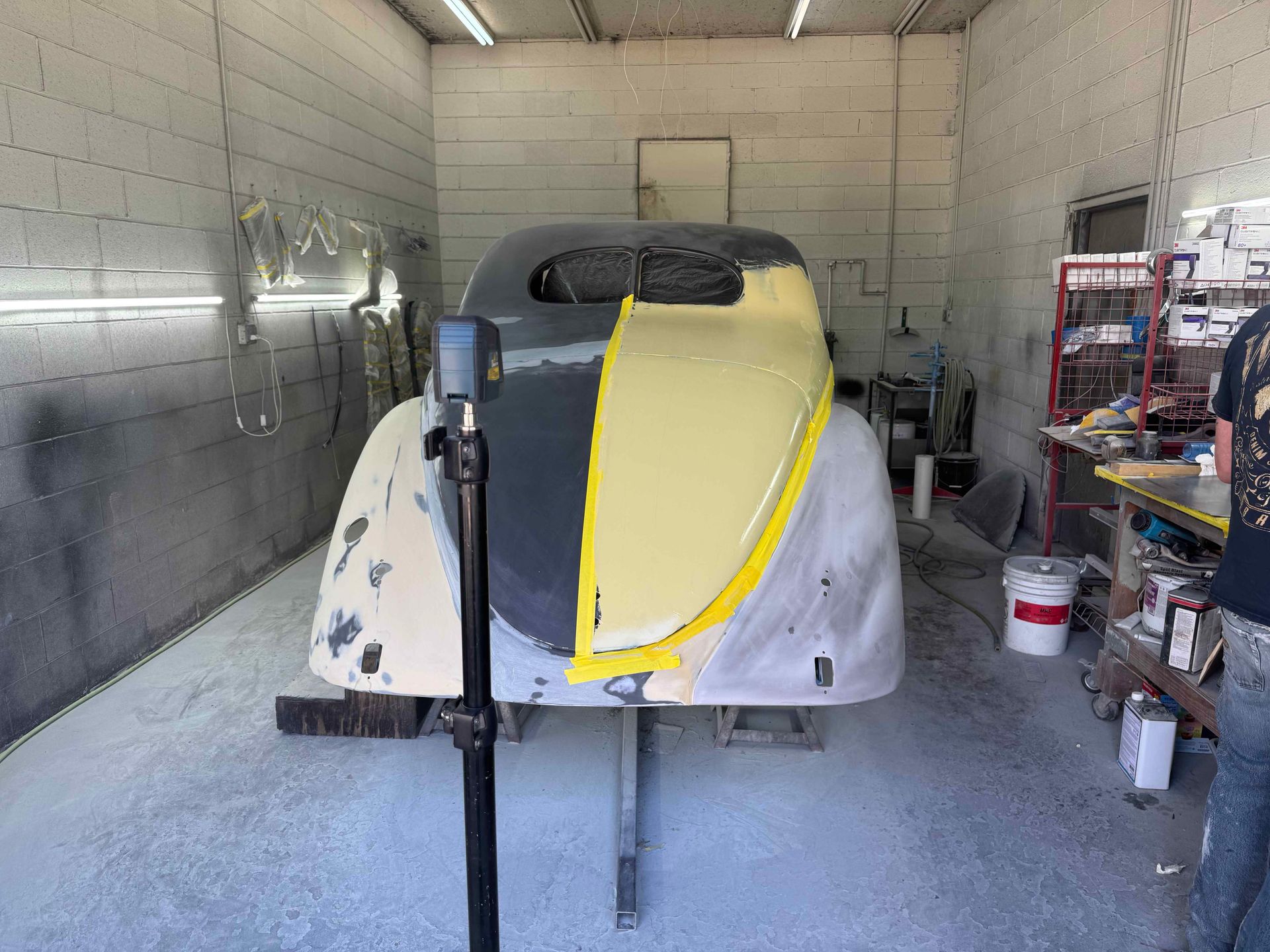 Small boat under construction in a workshop, with yellow tape on the bow and exposed fiberglass sides.