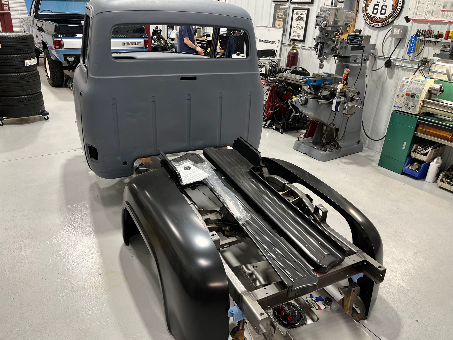 Gray vehicle cab and black chassis in an auto workshop, with tools and equipment around it