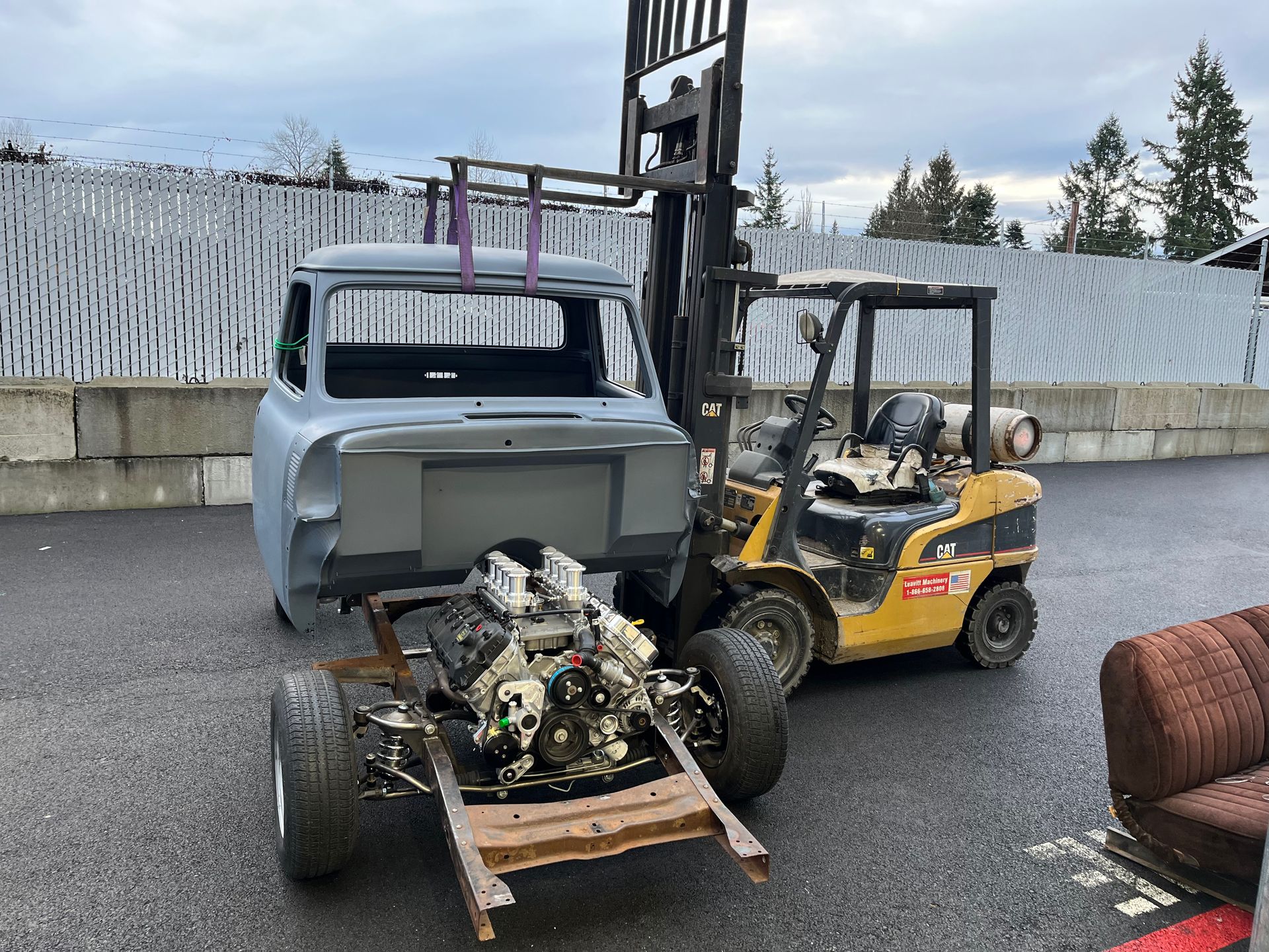 Forklift towing a truck cab and engine on a trailer in an outdoor yard