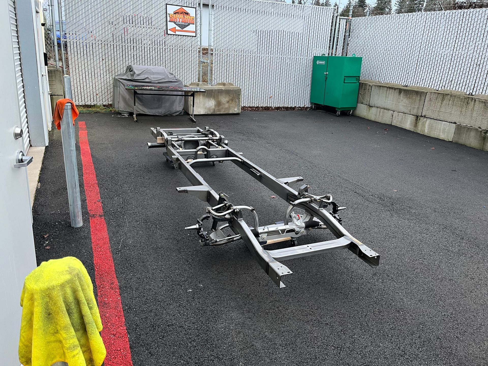 Boat trailer in a narrow paved lane beside a wall, with red curb line and green bin at the end.