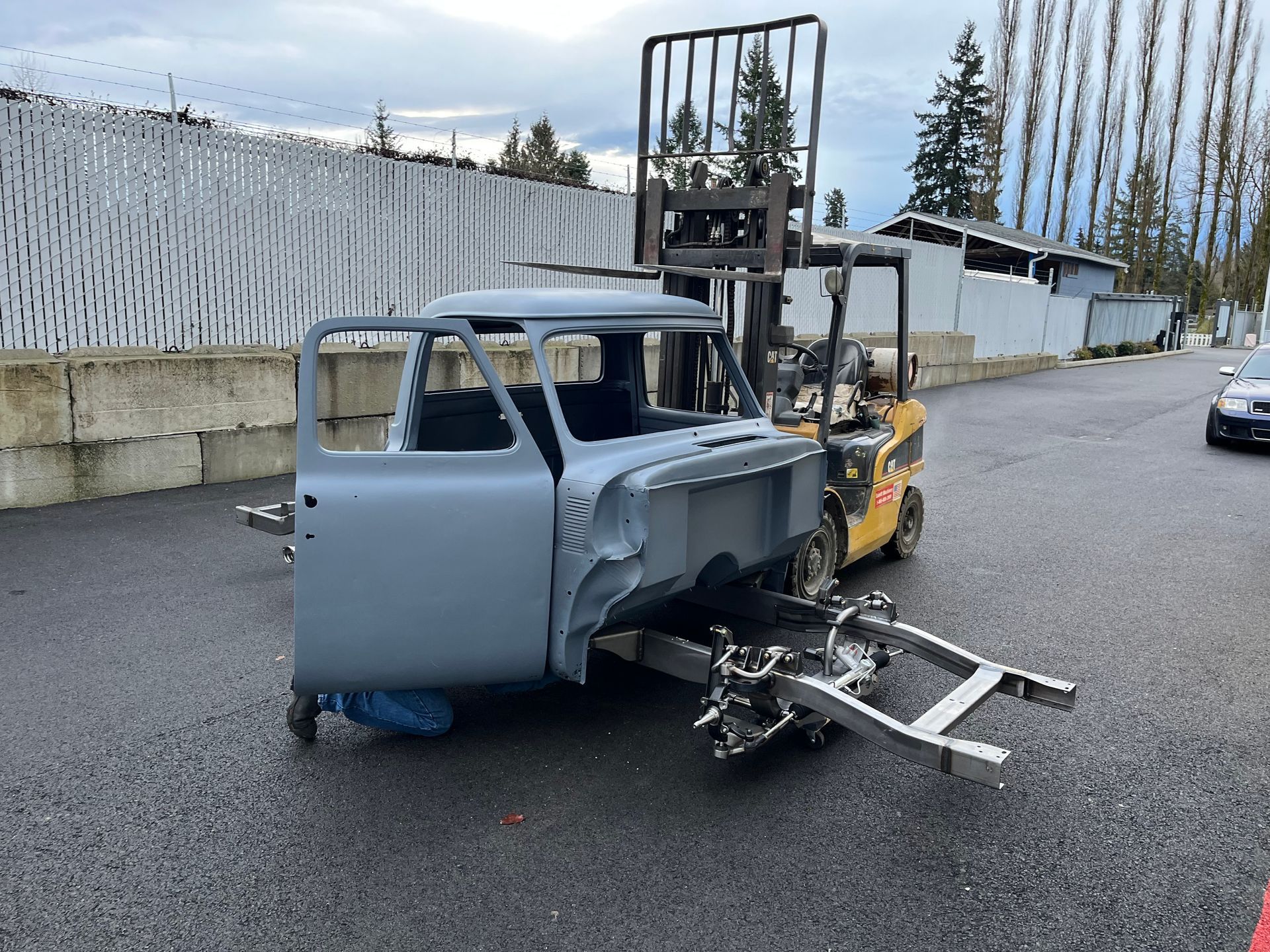 Damaged gray forklift and stripped car body on pavement outside a warehouse