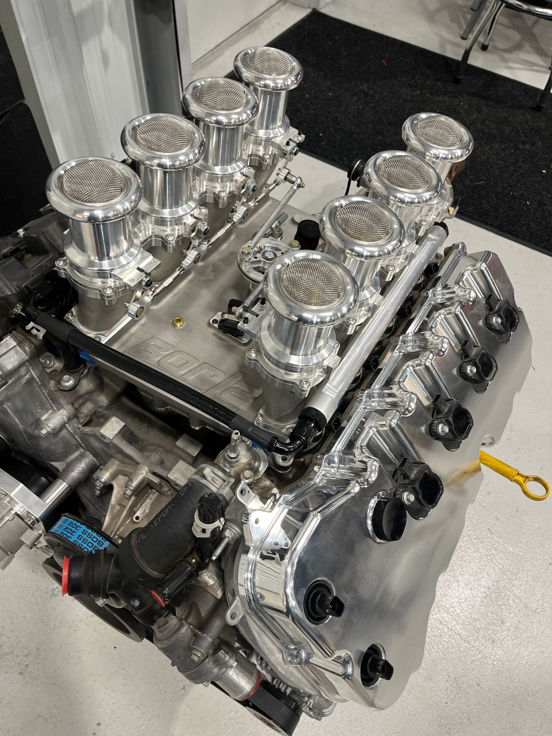 Polished V8 engine on a workshop floor, with shiny carburetors and visible black ignition wiring.