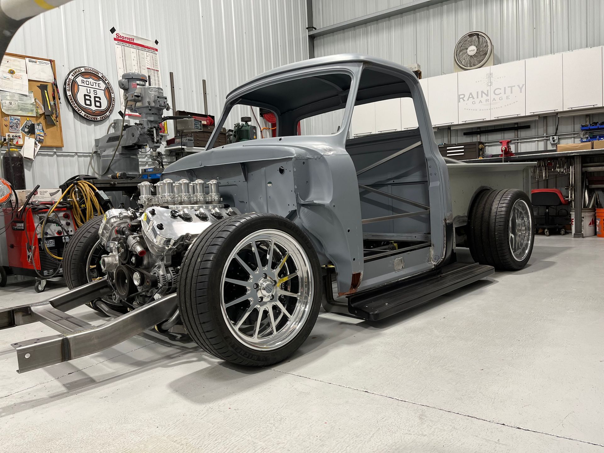 Gray custom hot rod chassis in a workshop, with exposed engine and large rear wheels, side view