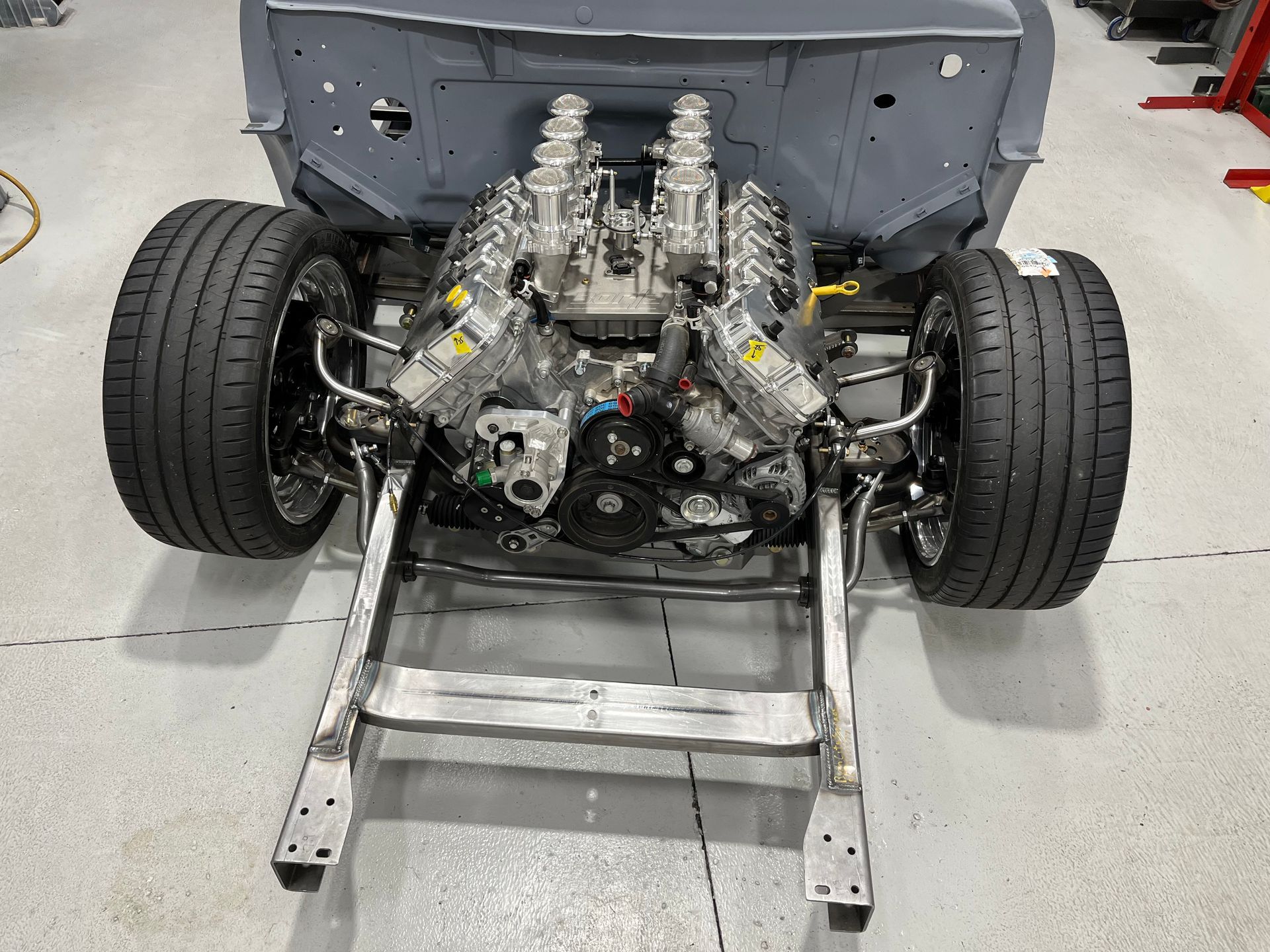 Rear view of a car chassis with exposed engine and suspension on a workshop floor.