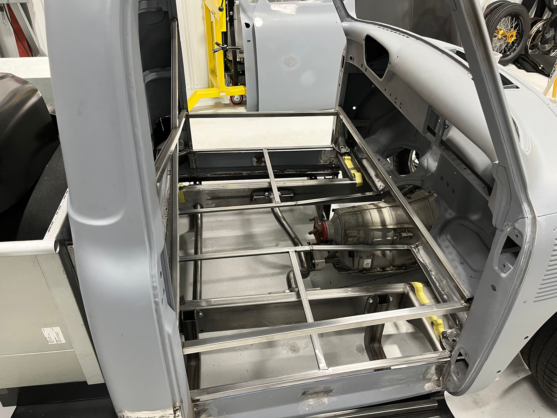 Exposed car interior with seats removed, showing metal floor frame and open side paneling