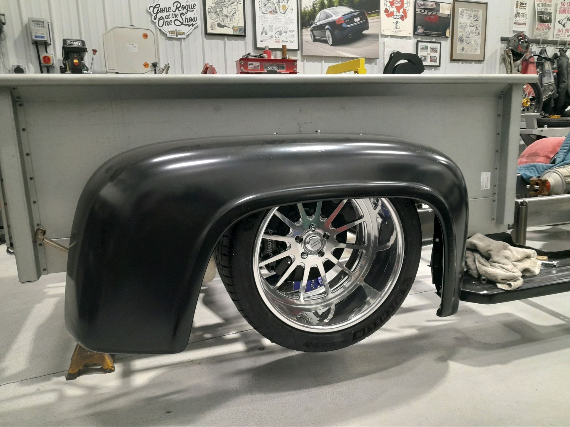 Black custom car fender over a chrome wheel in a workshop, with shelves and tools in the background