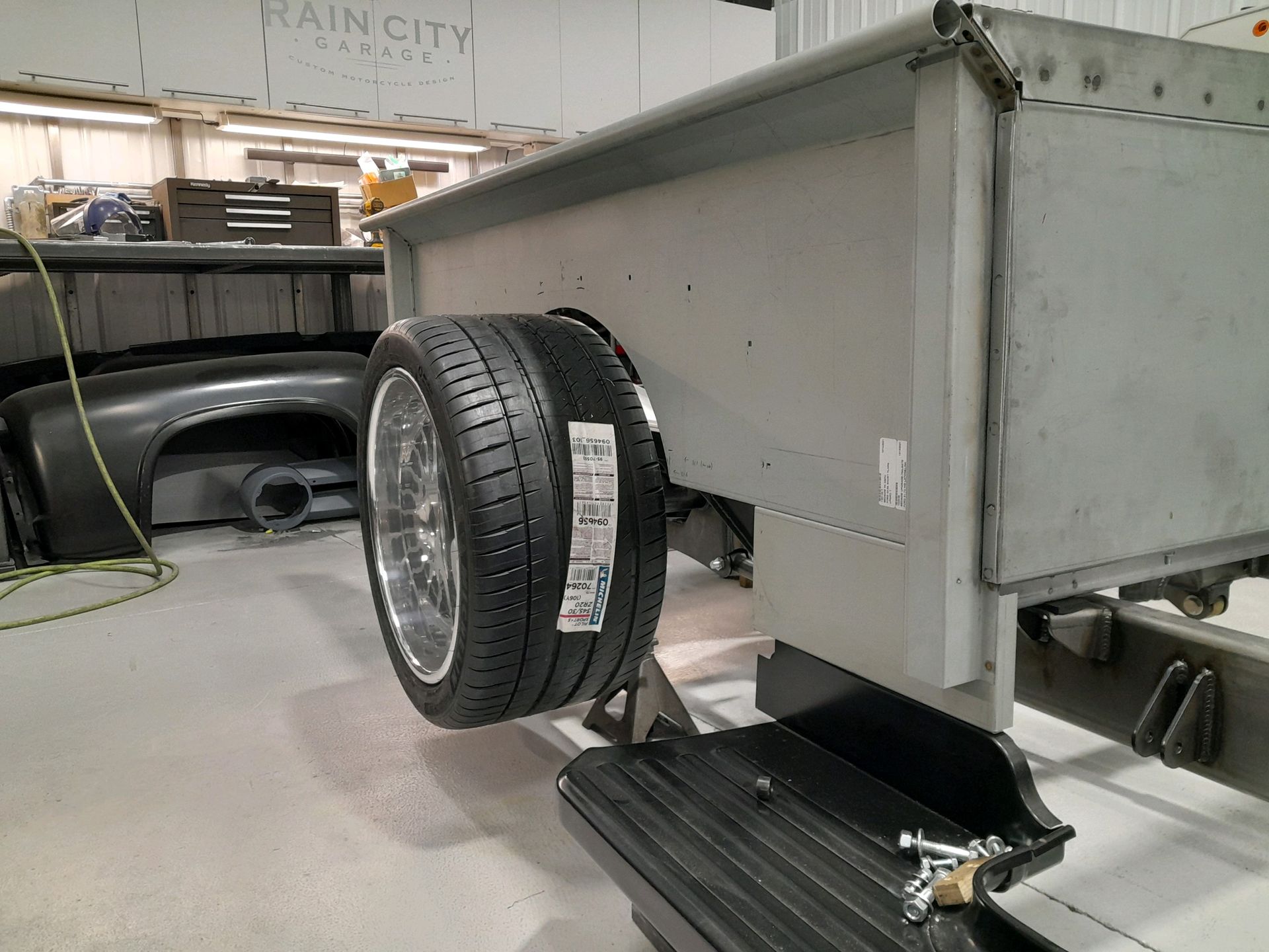 White trailer on jack with spare tire mounted underneath in a workshop/garage