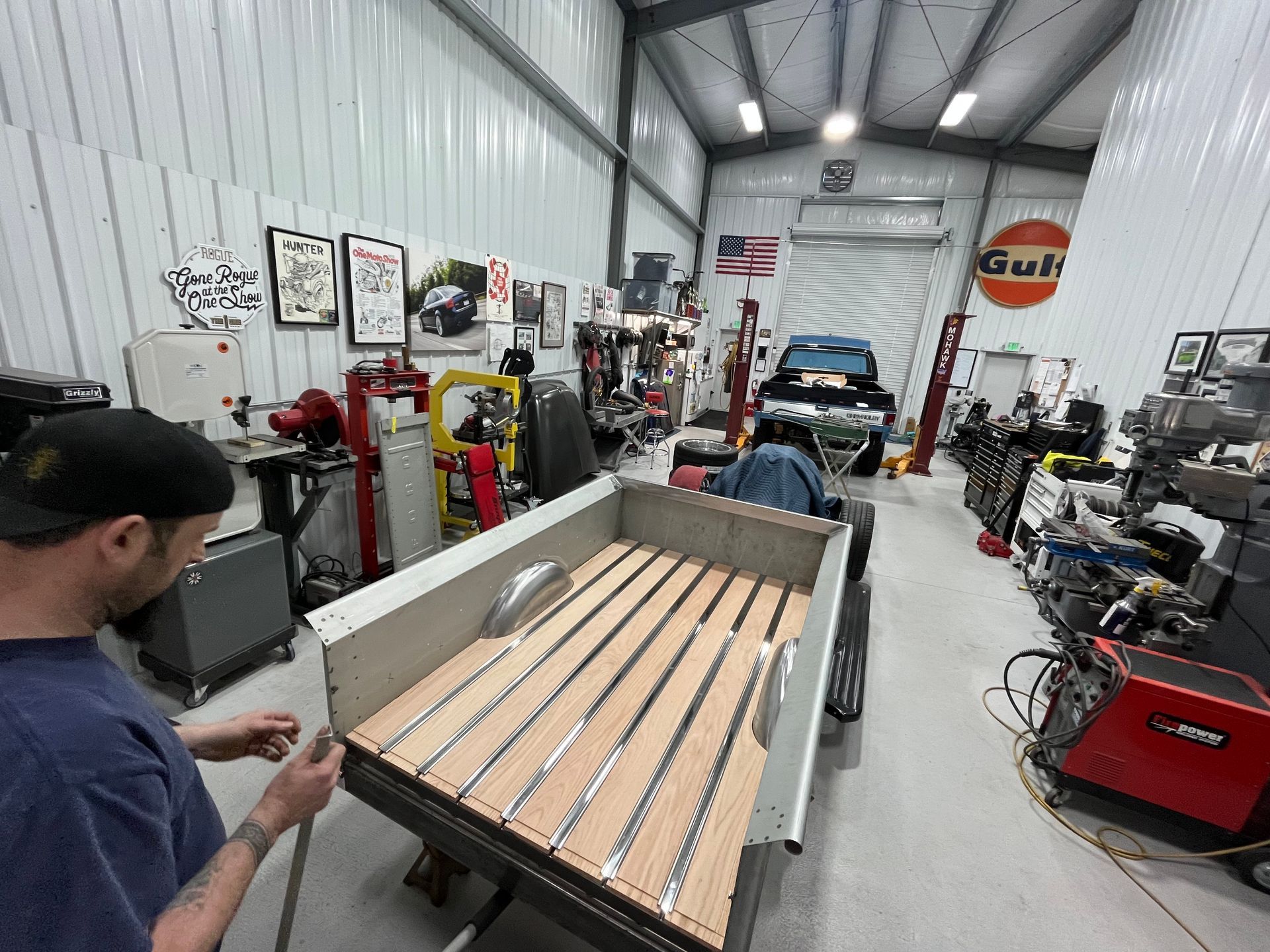 Auto shop interior with a worker adjusting a large wooden board on a rolling cart.