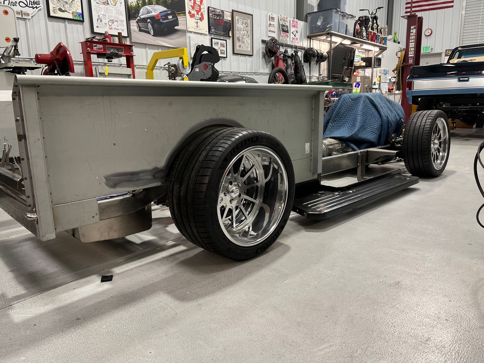 Custom gray hot rod chassis with exposed wheels in a garage workshop