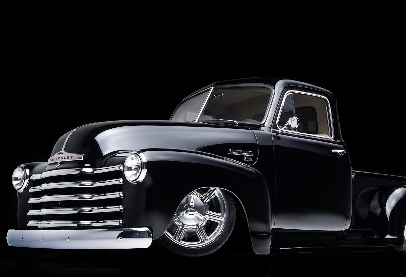 Black vintage pickup truck with chrome grille and custom wheels on a dark background