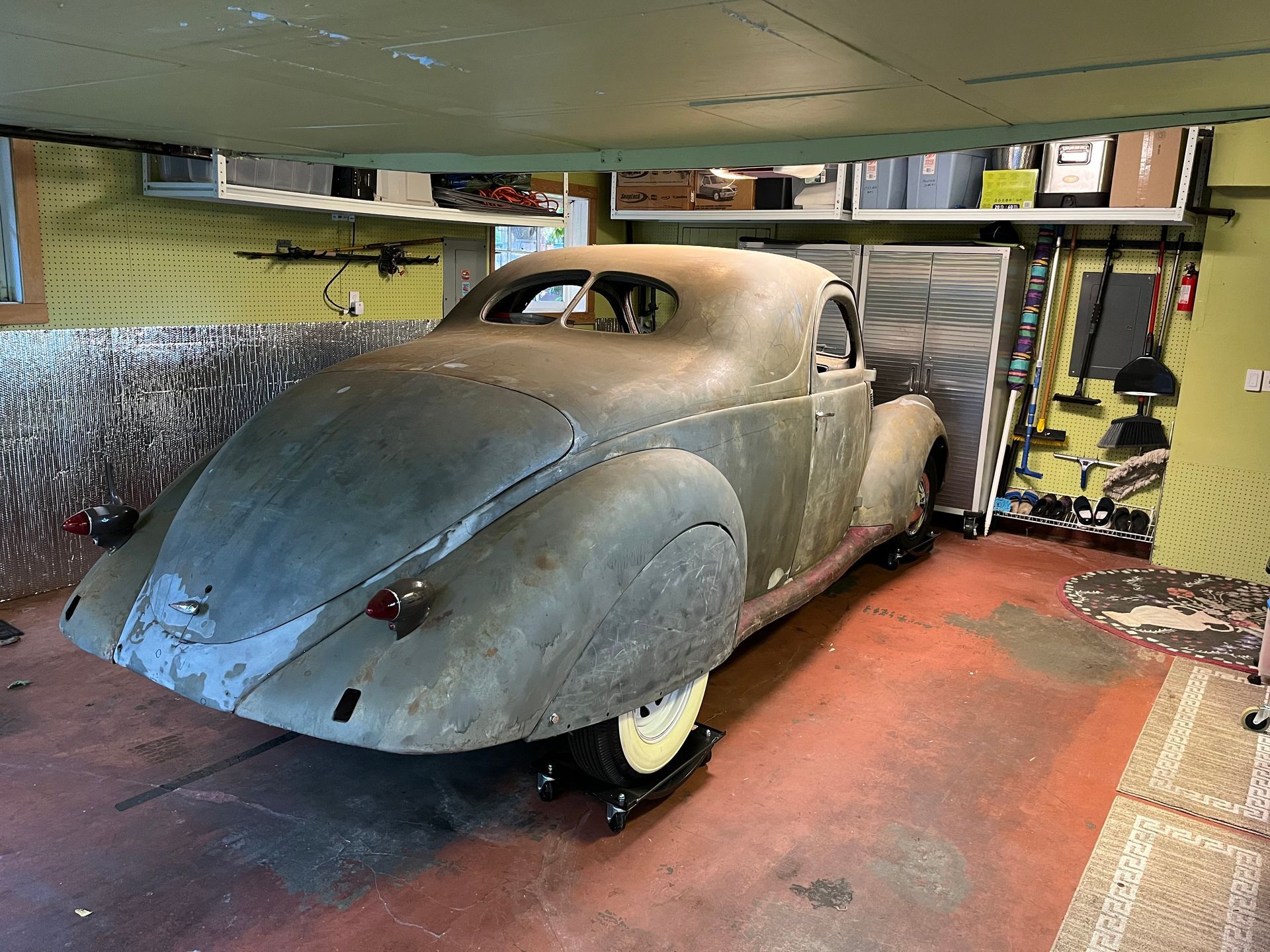 Vintage gray car in a cluttered garage, seen from the rear-left side.