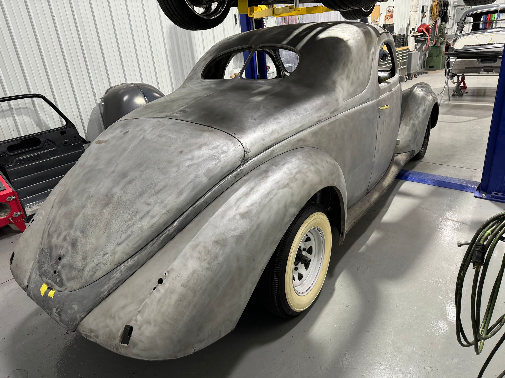 Gray vintage race car body in a workshop, shown from the rear-left side.