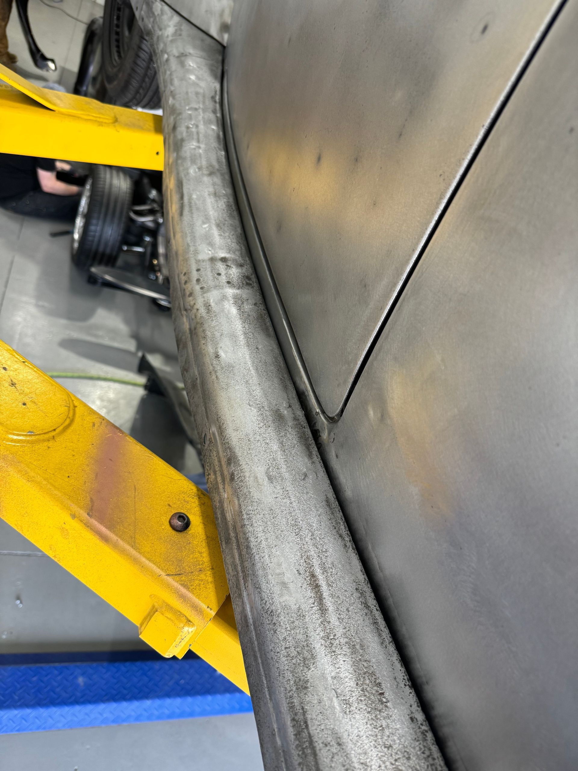 Close-up of a worn black rubber conveyor belt beside yellow metal machinery and a gray wall.