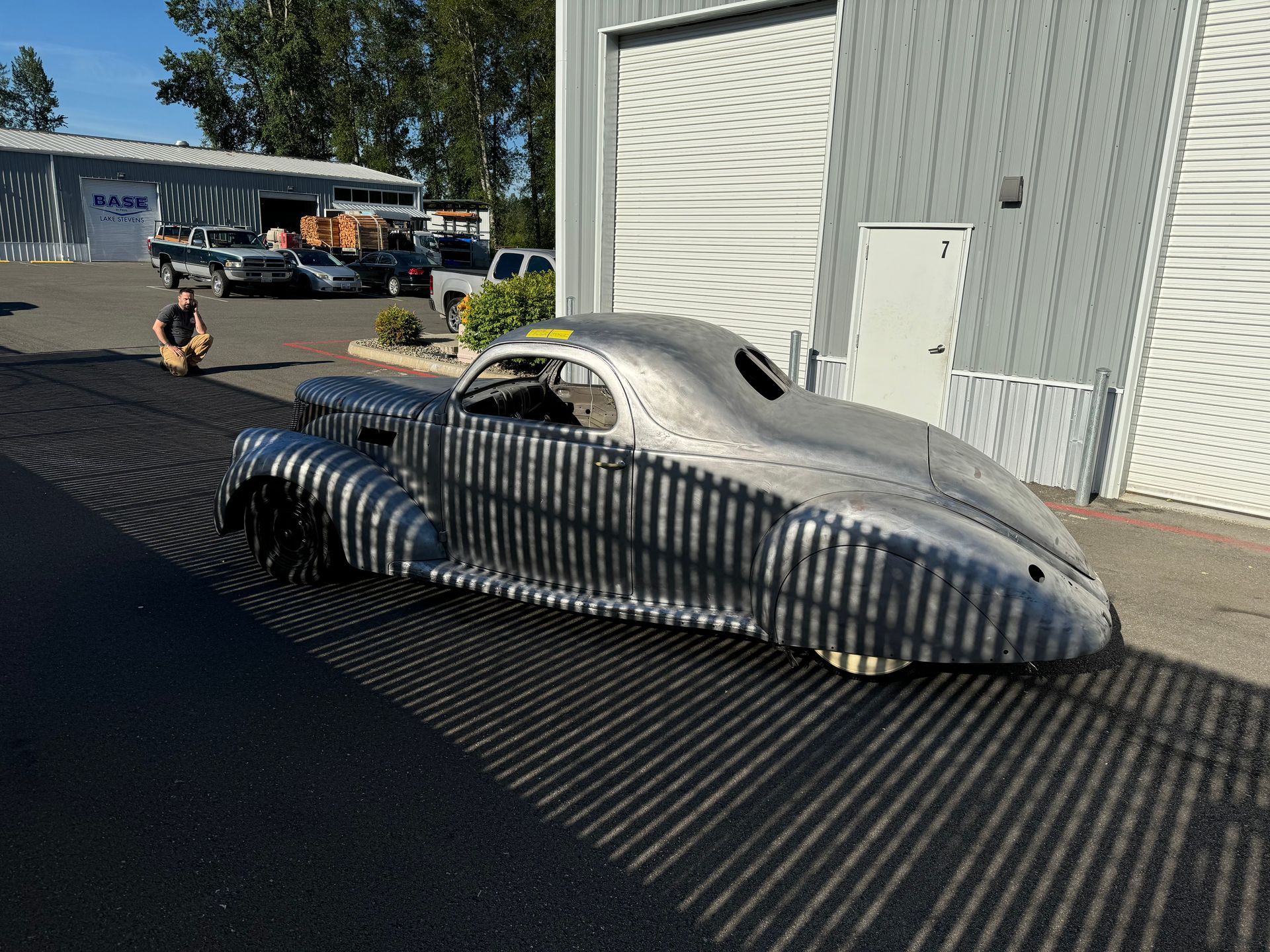 Silver streamlined car sculpture on a black paved lot beside a corrugated metal building