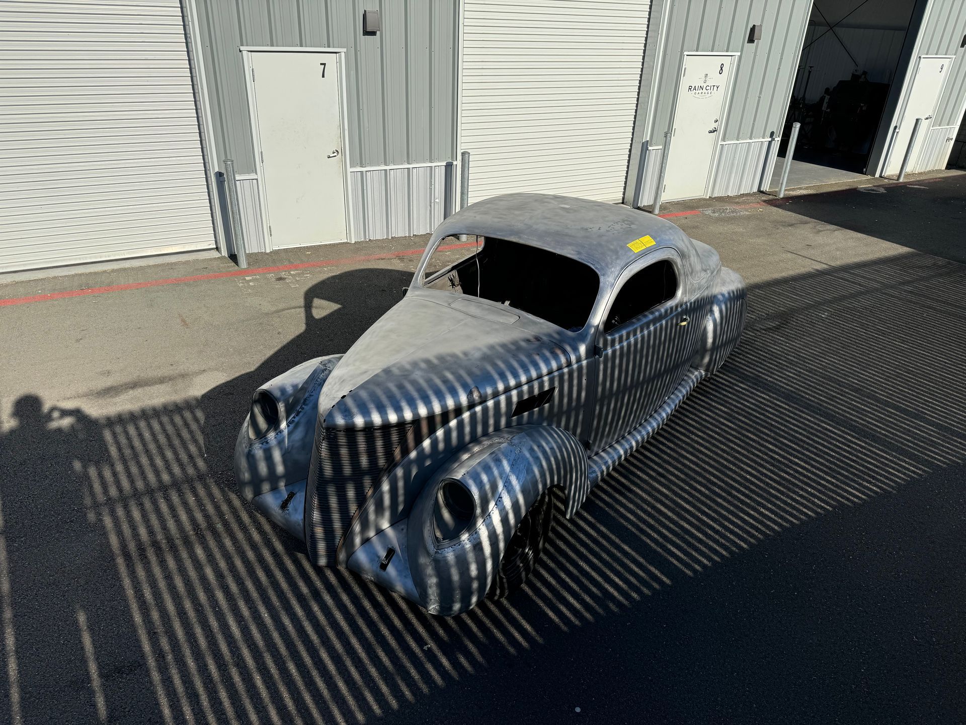 Shiny silver vintage coupe parked outside a garage in bright sunlight
