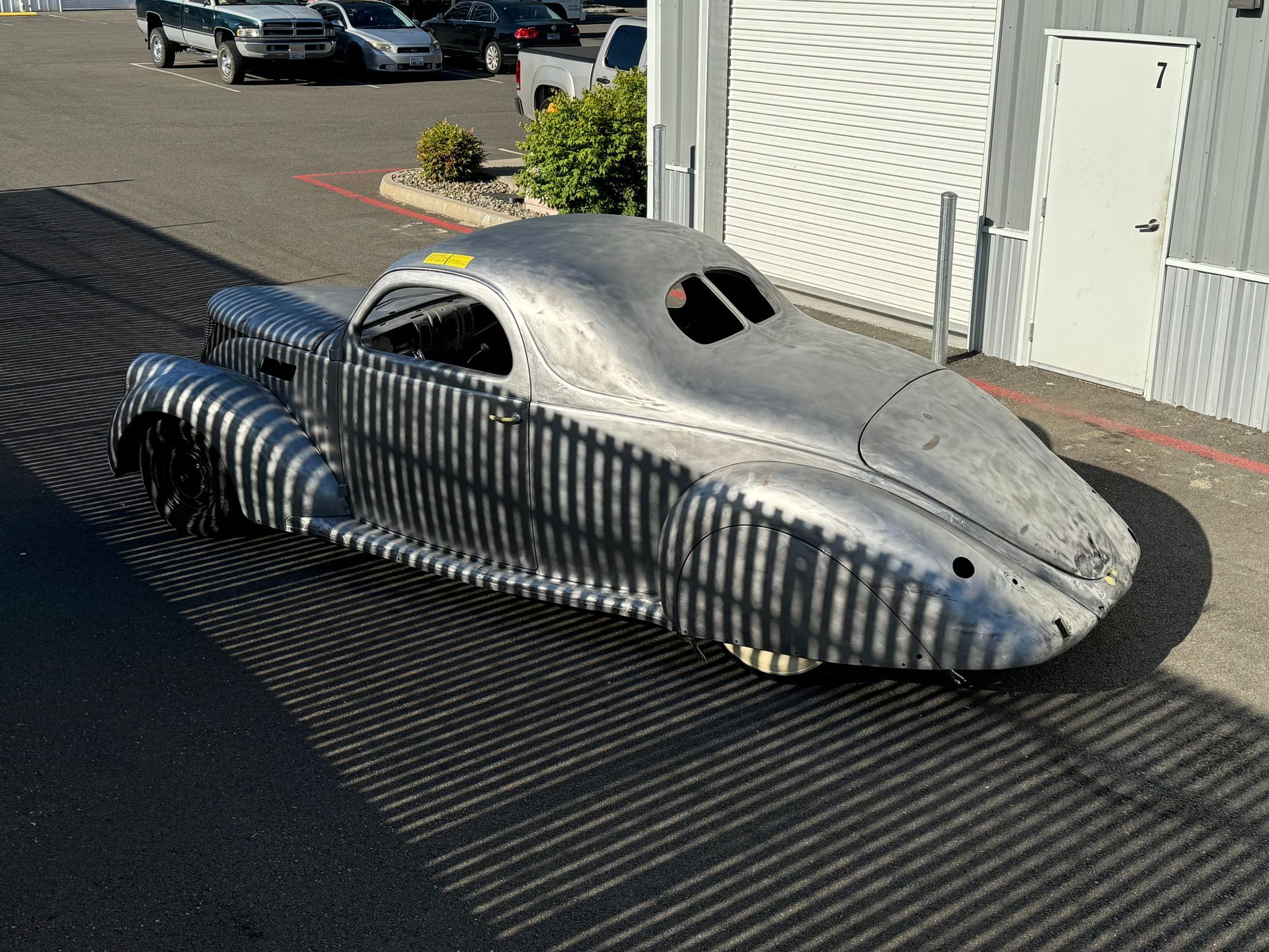 Striped silver retro-style vehicle with a covered cockpit parked on a paved lot.