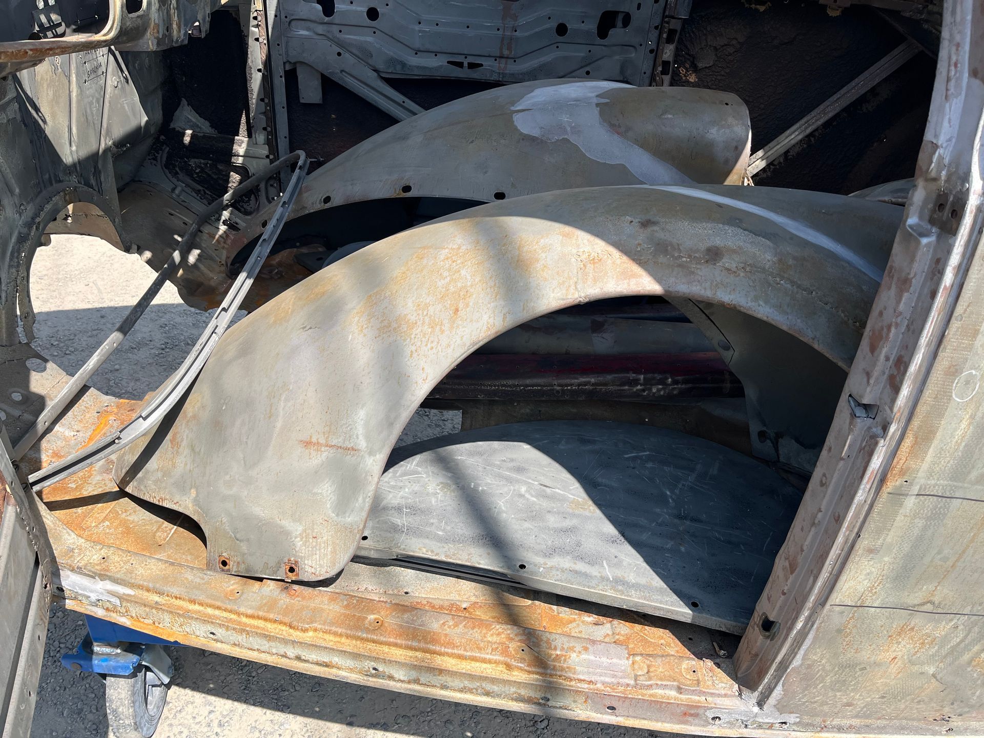 Rusty old metal fender inside a stripped vehicle frame, with curved wheel arch in a damaged workshop setting