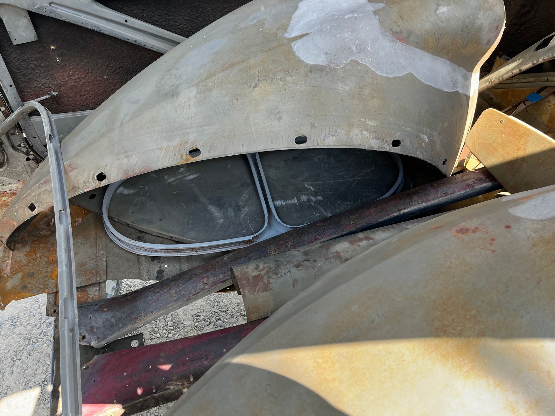 Scuffed metal and plastic parts piled in a cluttered junkyard, with a dark car seat visible underneath