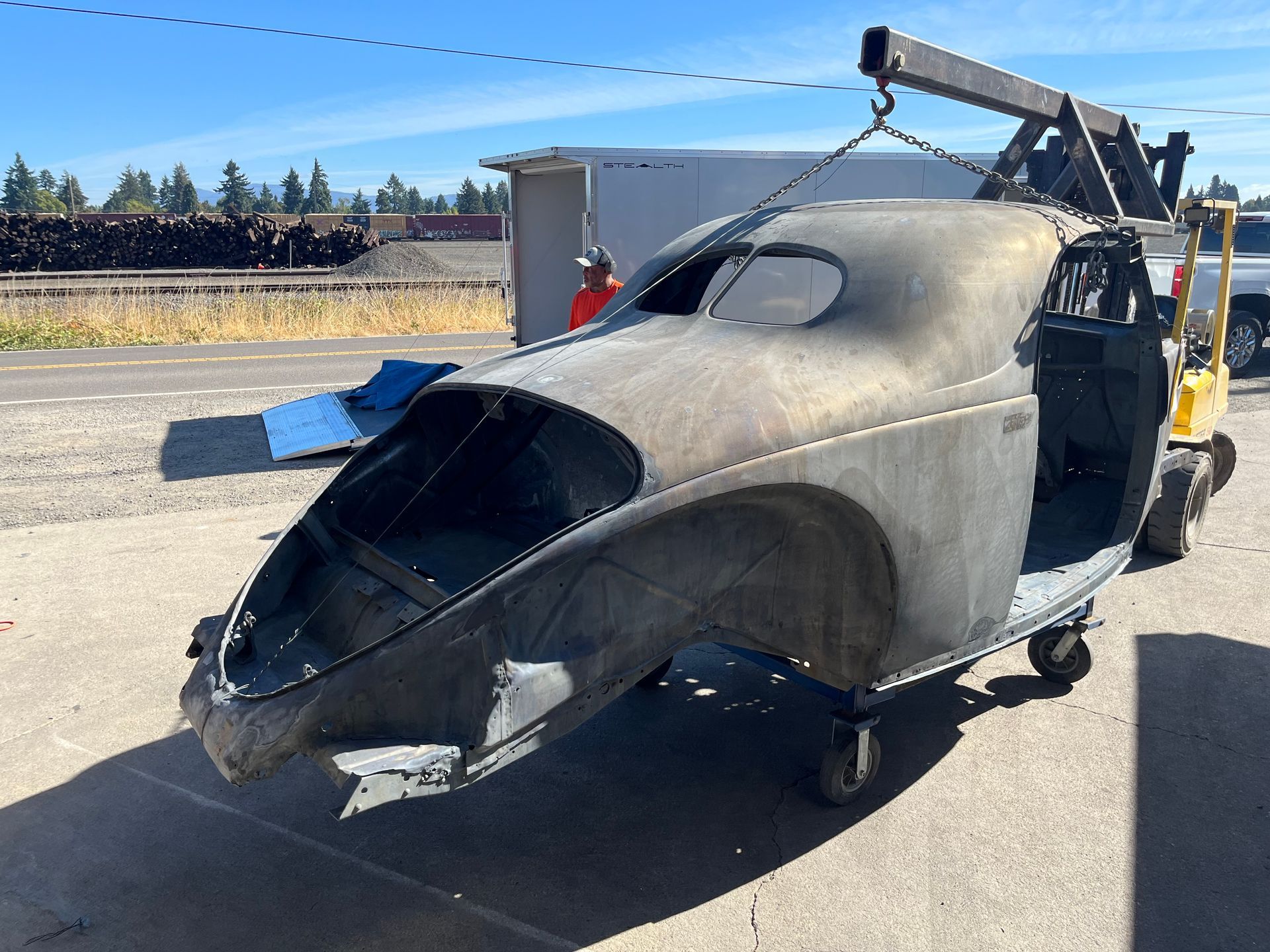 Damaged black helicopter fuselage with open side, parked on a tarmac near a white truck