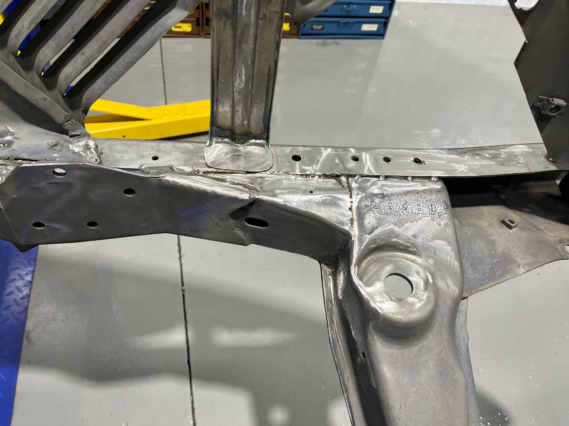 Close-up of a metal vehicle frame being repaired, showing welded silver and black parts.