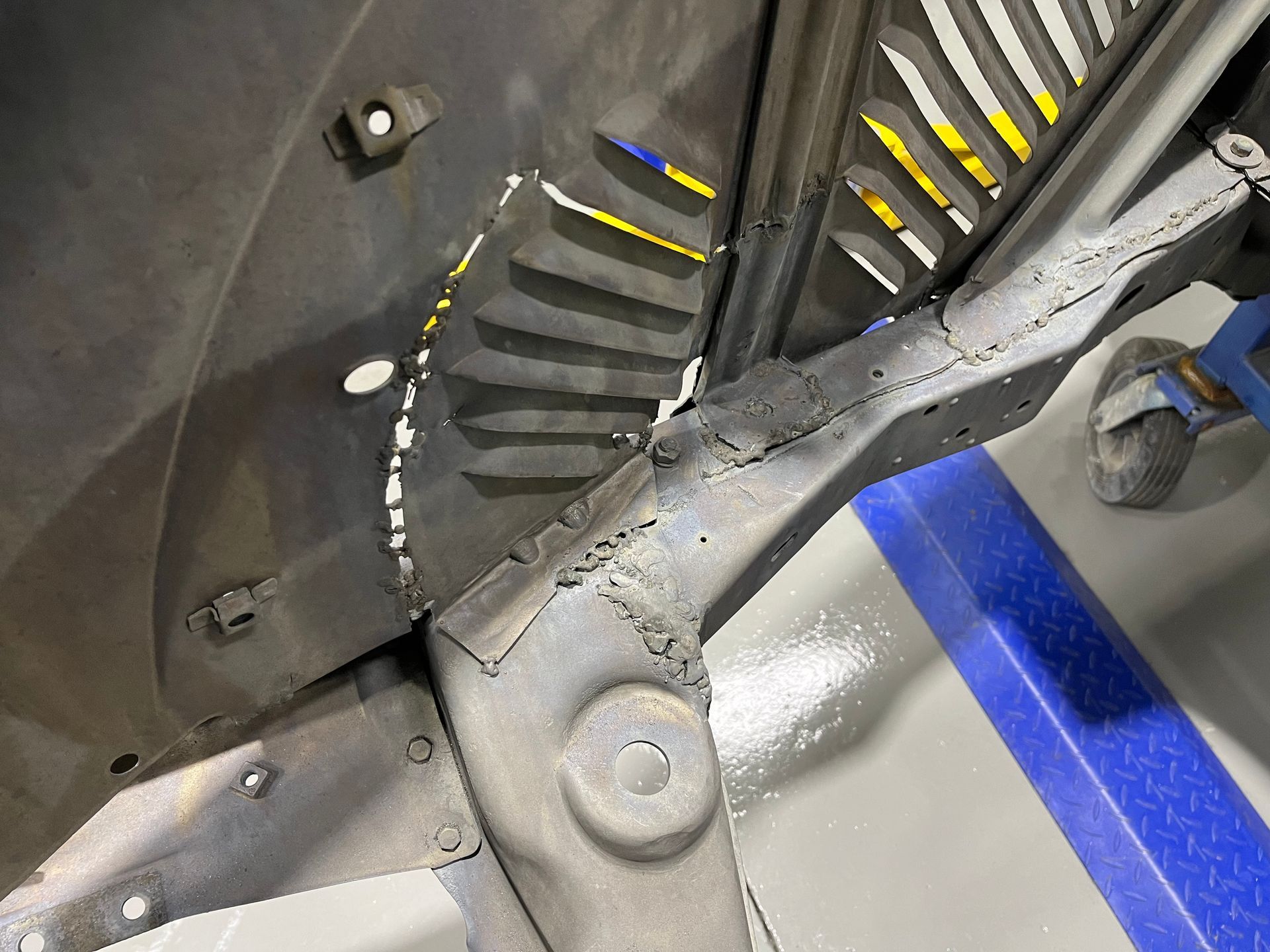 Close-up of a car wheel well with black and gray components, yellow-striped vents, and blue tape on the floor