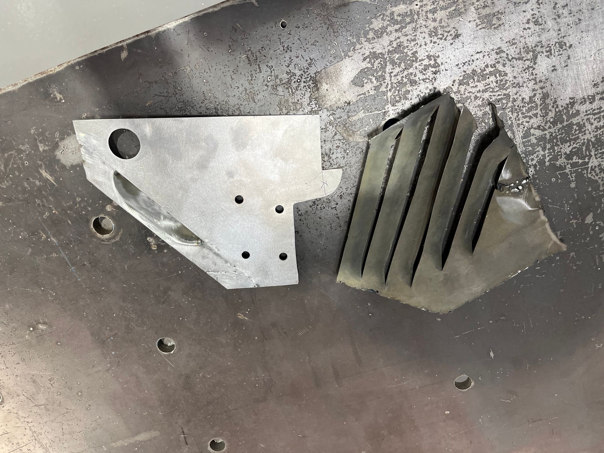 Close-up of two metal brackets with holes and ridges on a scratched gray surface
