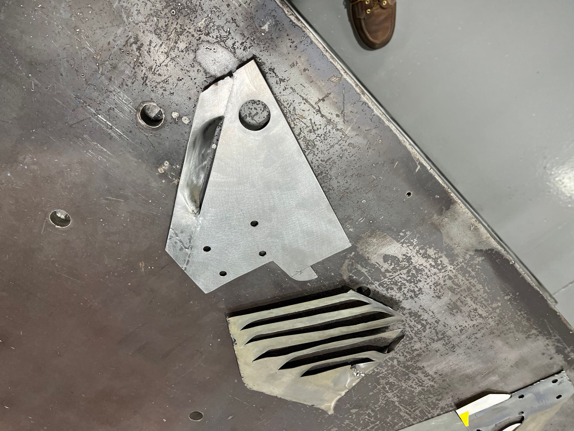 Close-up of a worn metal floor panel with a vent and bolts, showing scuffs and grime.