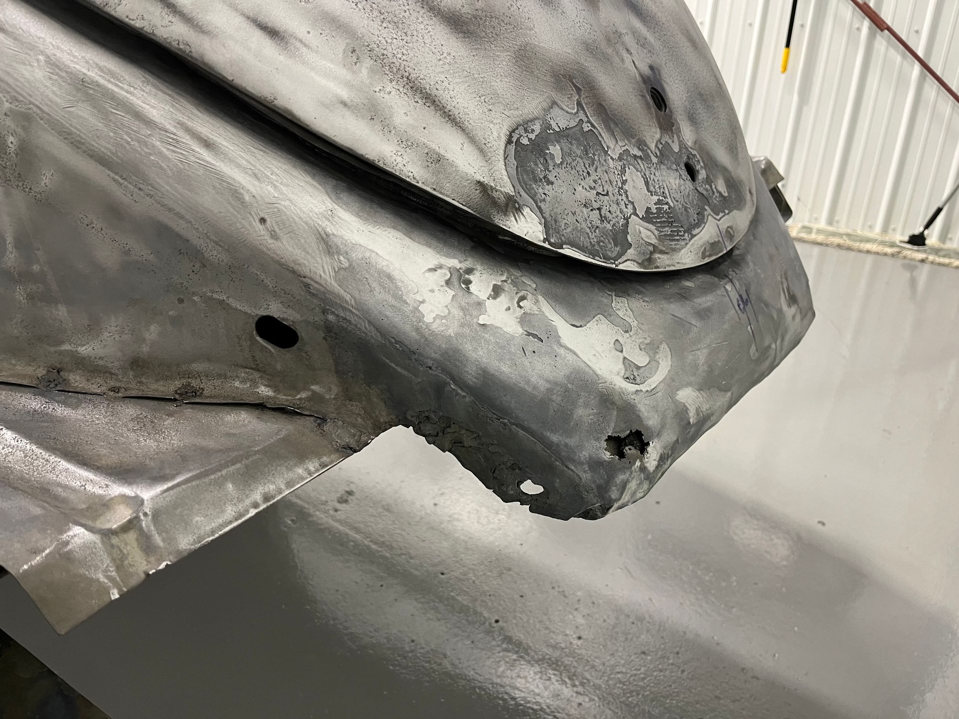 Close-up of a damaged gray car bumper and fender with scraped paint in a repair shop
