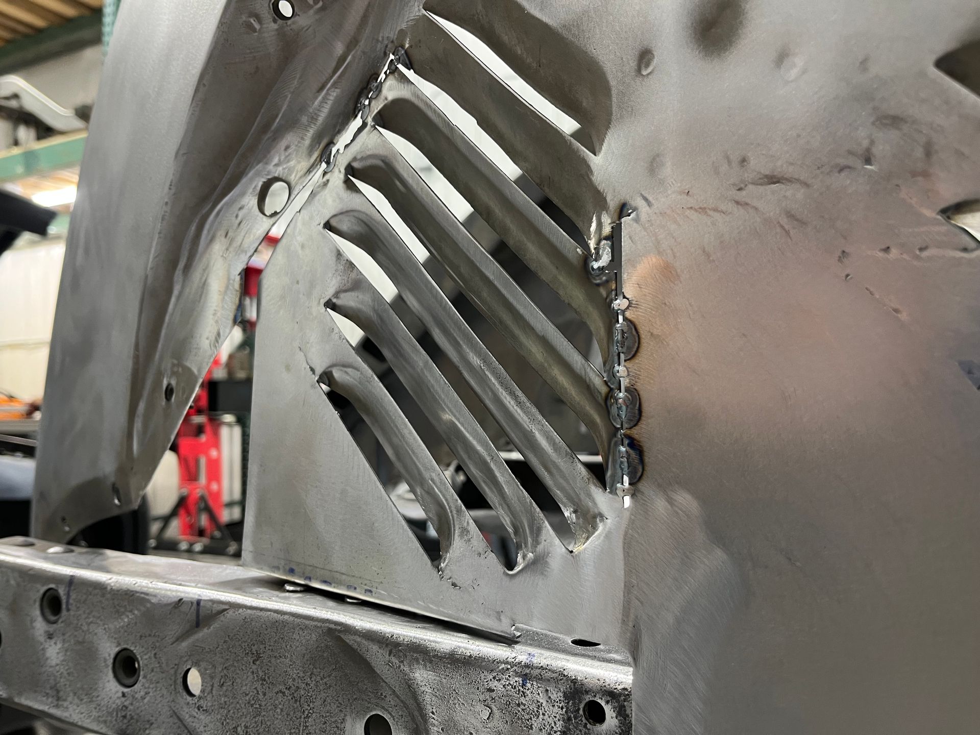 Close-up of a black metal vehicle panel with diagonal vents and bolts in an industrial setting