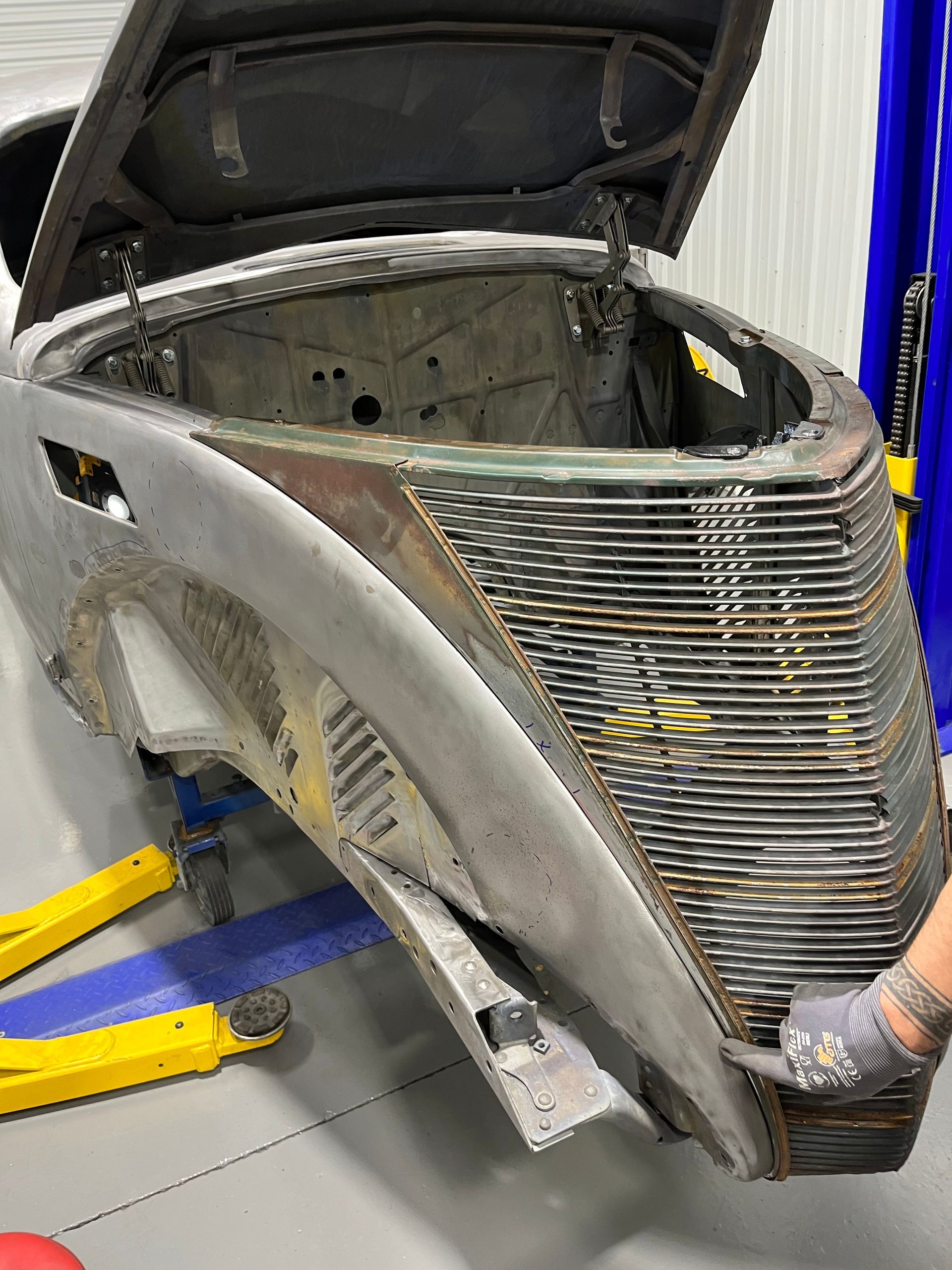 Classic car body shell on a lift in a workshop, with front grille and hood open.