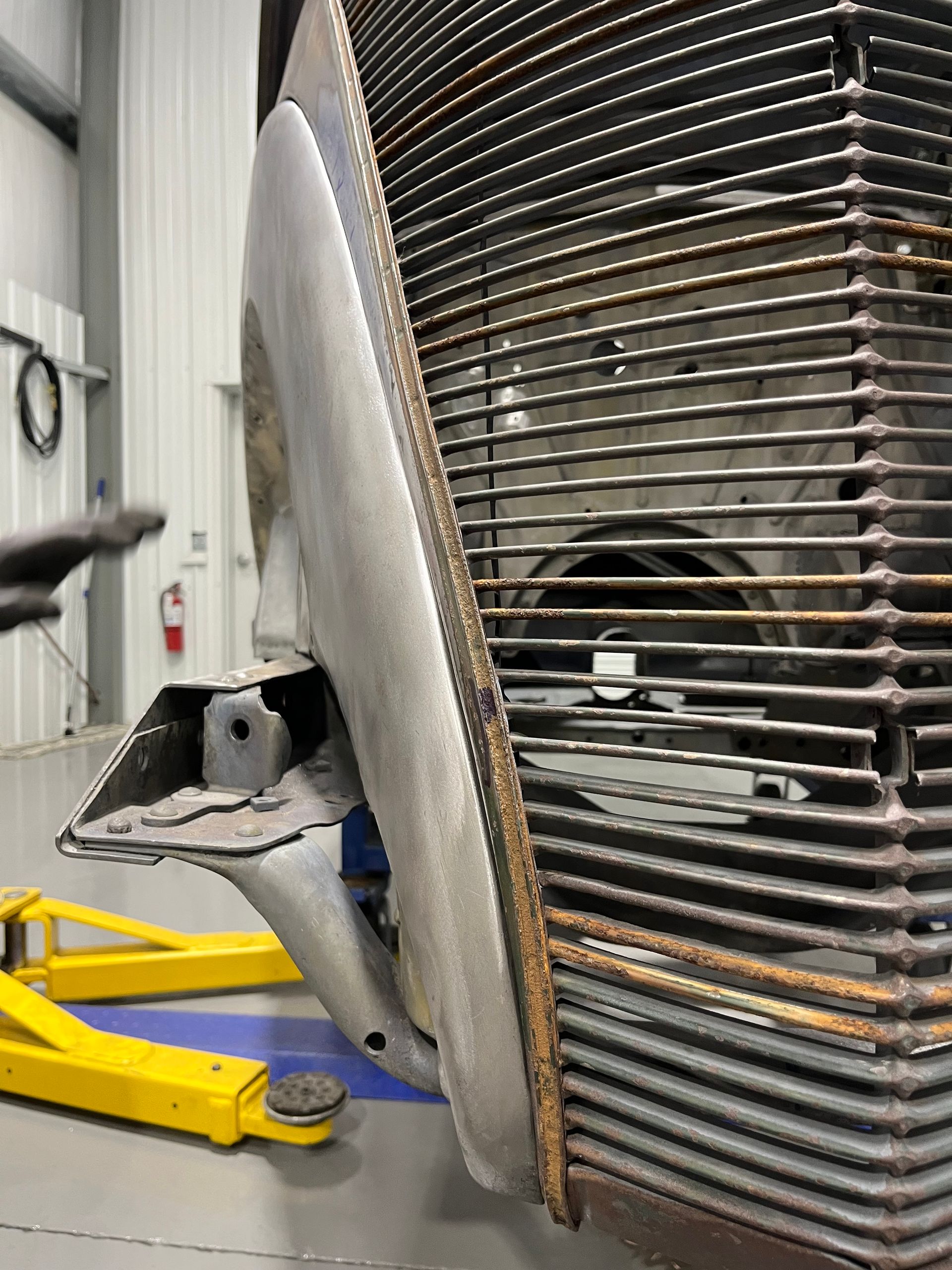 Damaged vehicle wheel and exposed suspension beside a large ribbed metal structure in a workshop