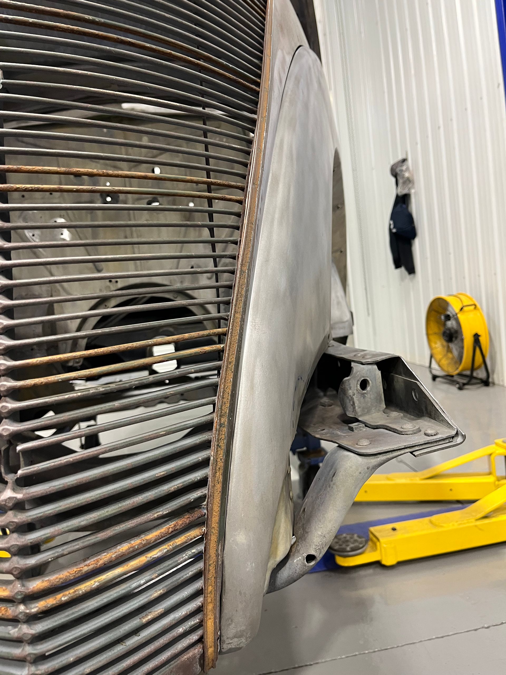 Damaged large metal structure in a workshop, with a torn panel and yellow floor jack nearby