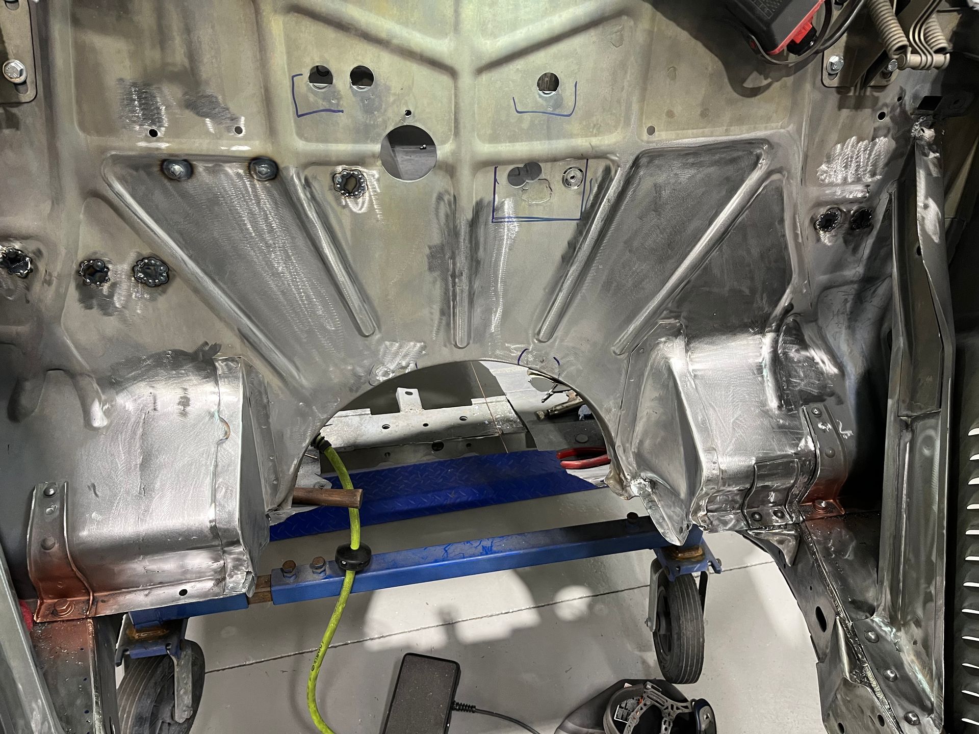 Bare metal car interior with exposed wheel arch, blue crossbar, and wiring during repair